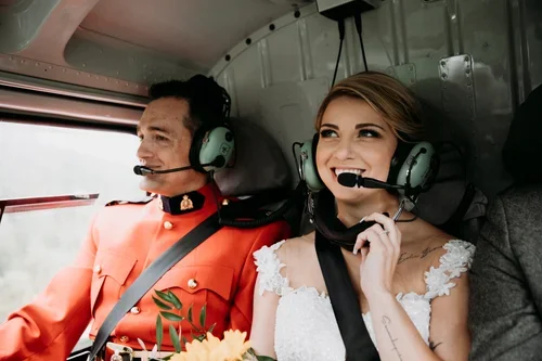 A man in a red uniform and a woman in a wedding dress wearing headsets inside a helicopter.