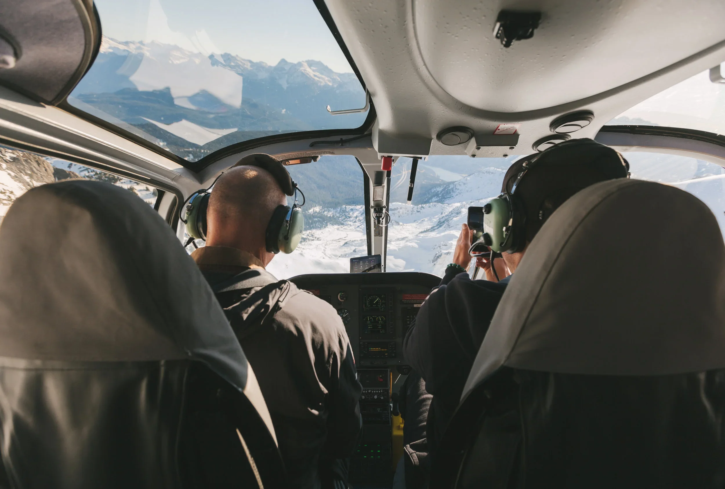 Rear view of passenger and pilot flying over scenic landscapes in a helicopter.