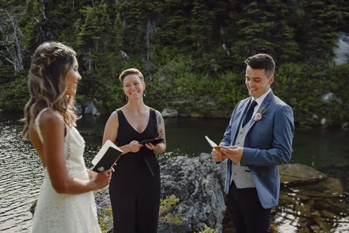A couple getting married outdoors by a river, with an officiant reading vows.