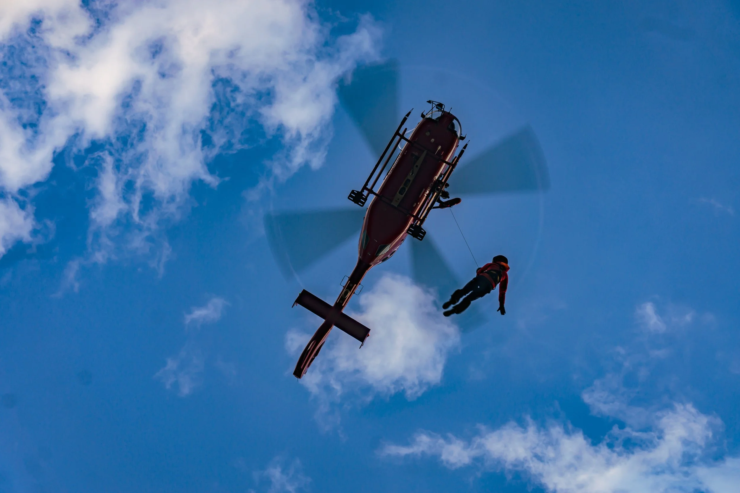 Red helicopter with Search and Rescue team member suspended below.