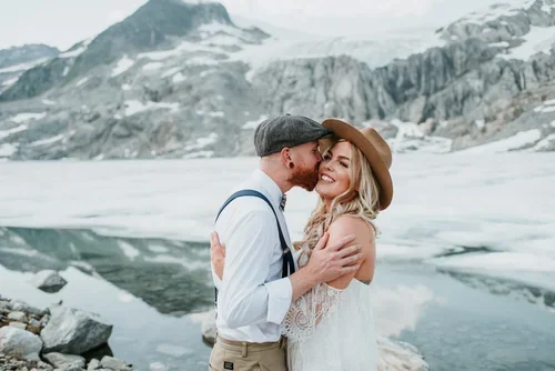 A couple embracing and smiling near a glacier with mountains in the background.