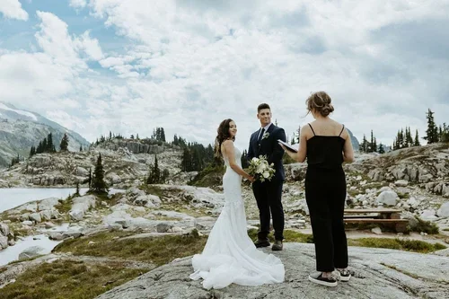 A couple getting married outdoors by a scenic mountain lake with an officiant.