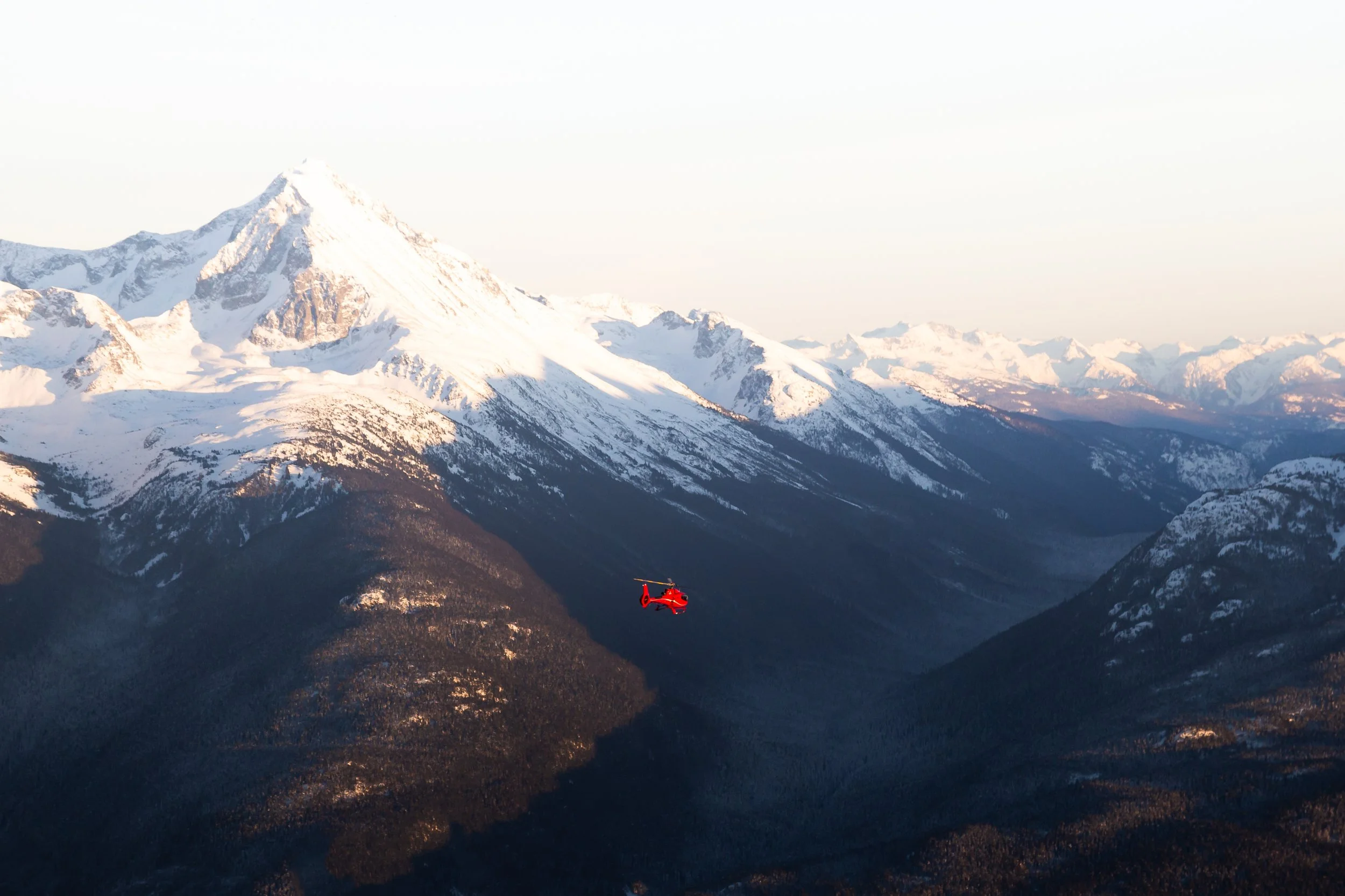 Red sightseeing helicopter flying through alpine mountain peaks.