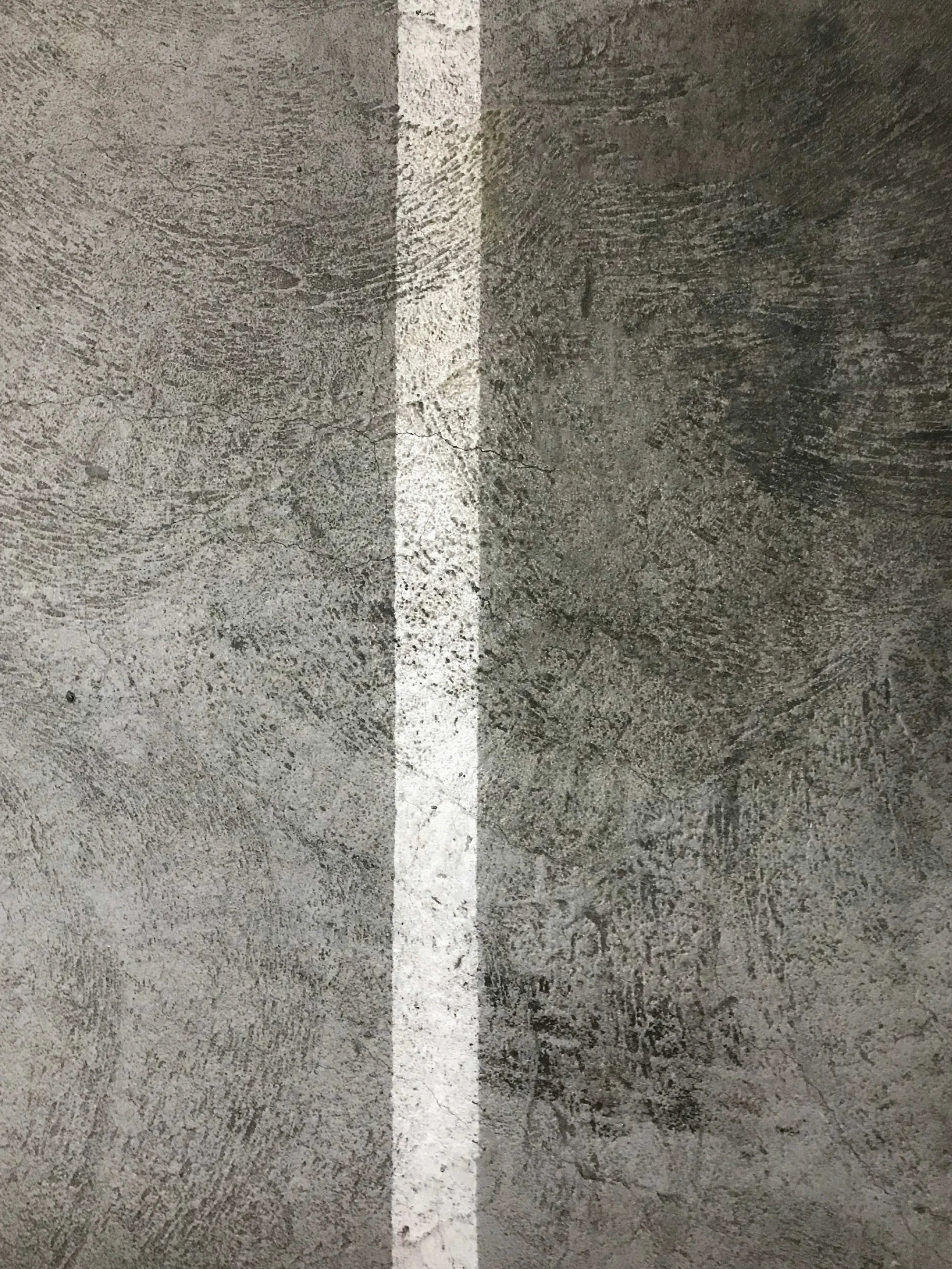 A close-up of a concrete parking lot surface with a single white line painted across it.