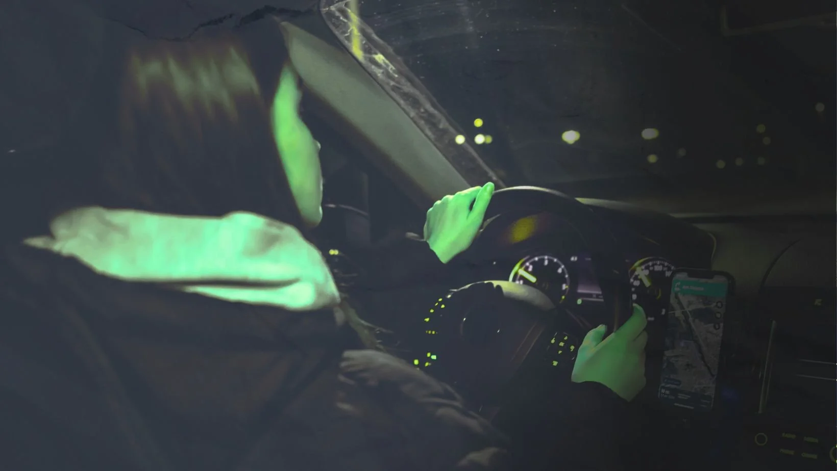 Person driving at night with city lights reflected across the windshield.