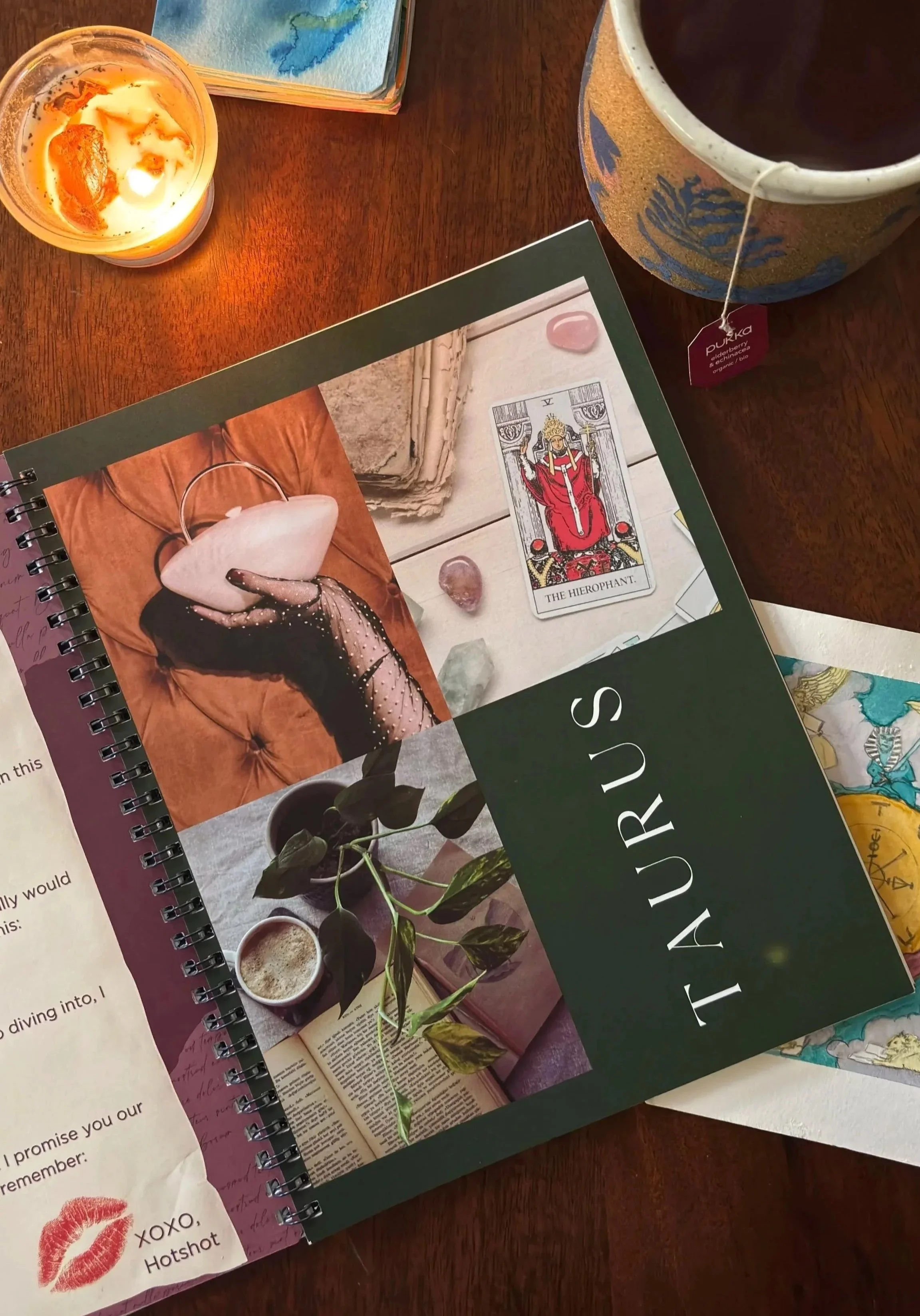 A top-down view of the Hidden Threads planner open to a 'Love Letter to Aries' page and Taurus transition, styled with tea and watercolor tarot decks.