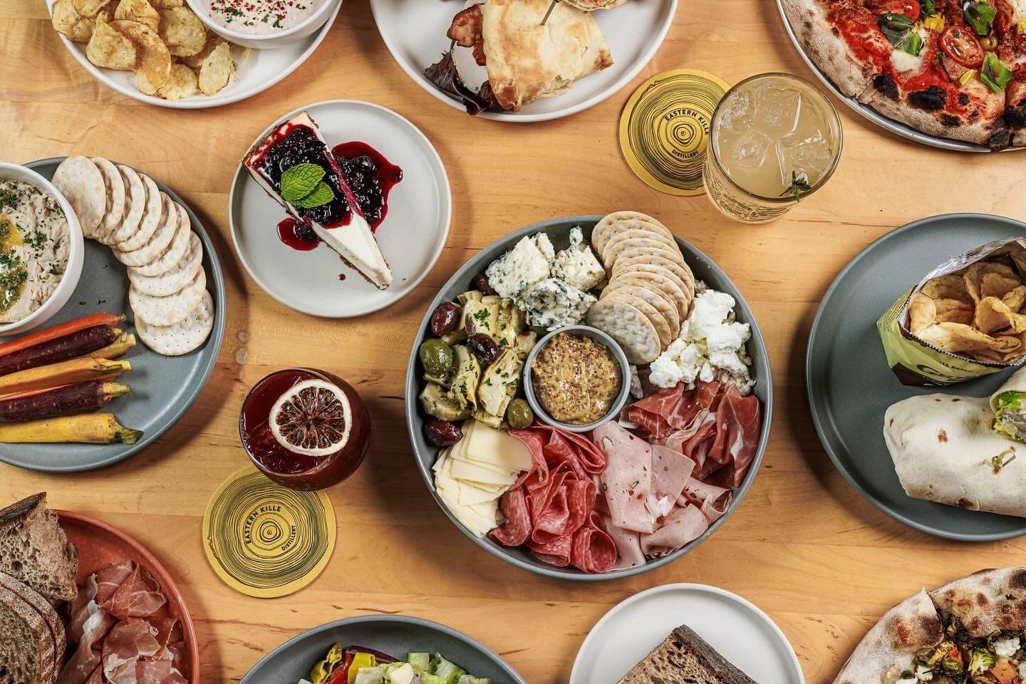 Variety of dishes on a wooden table including cheese, meats, vegetables, bread, pizza, and desserts.