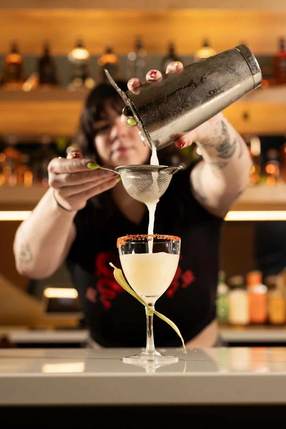Bartender pouring a cocktail through a strainer into a glass with a salted rim.