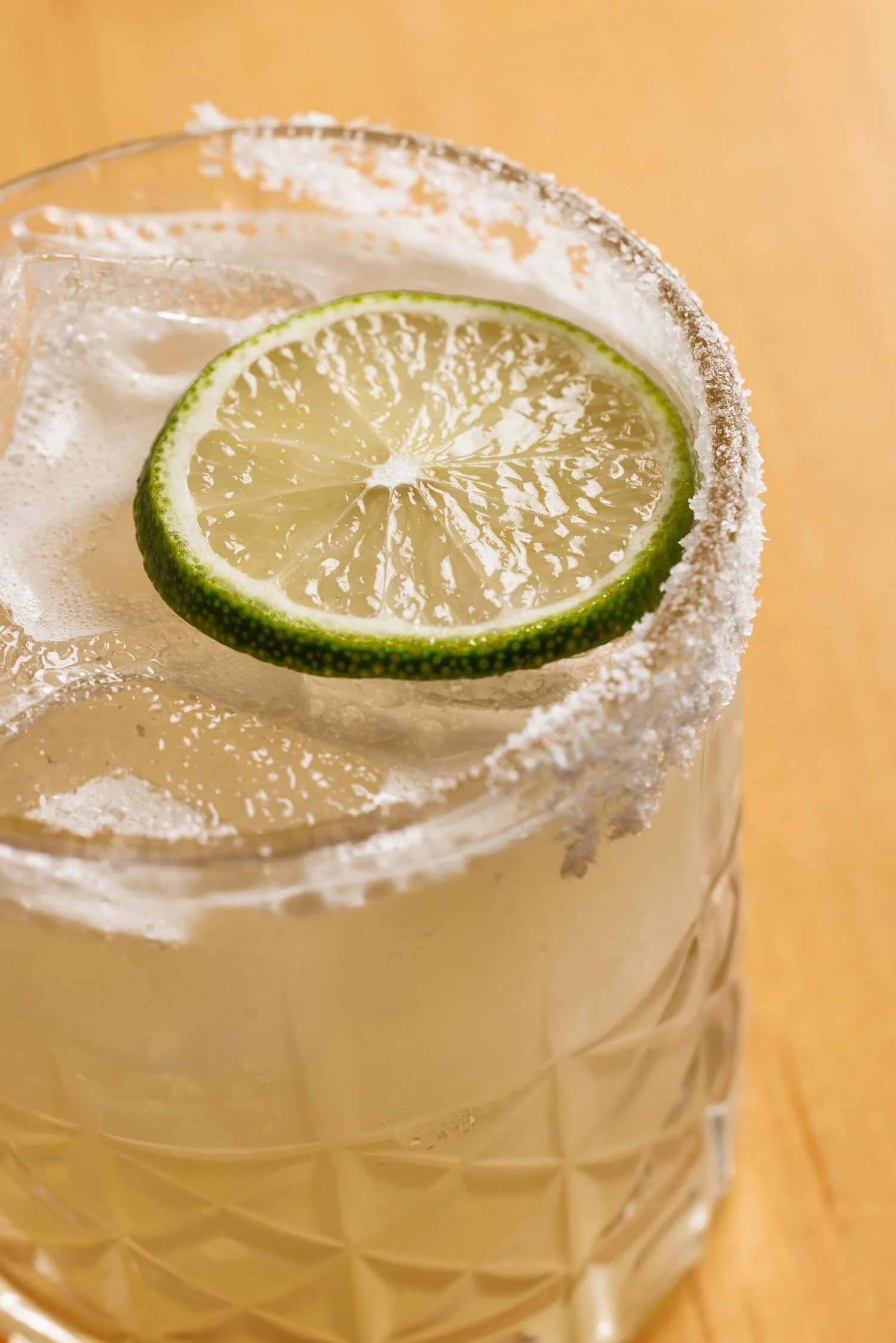 Close-up of a glass with salt-rimmed edge, containing a lime slice inside, on a wooden surface.