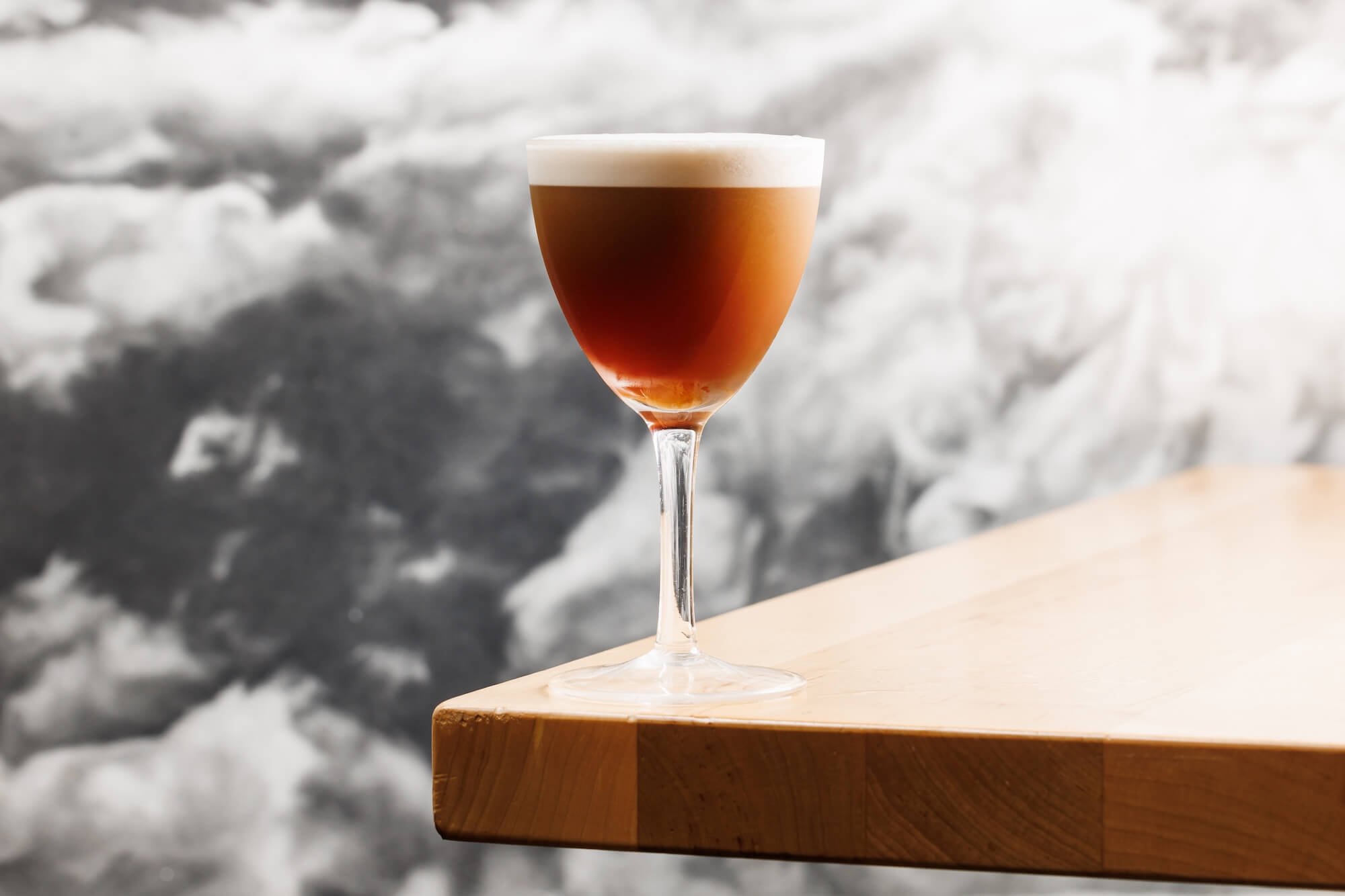 A glass of layered coffee beverage on a wooden surface with a blurred icy background.