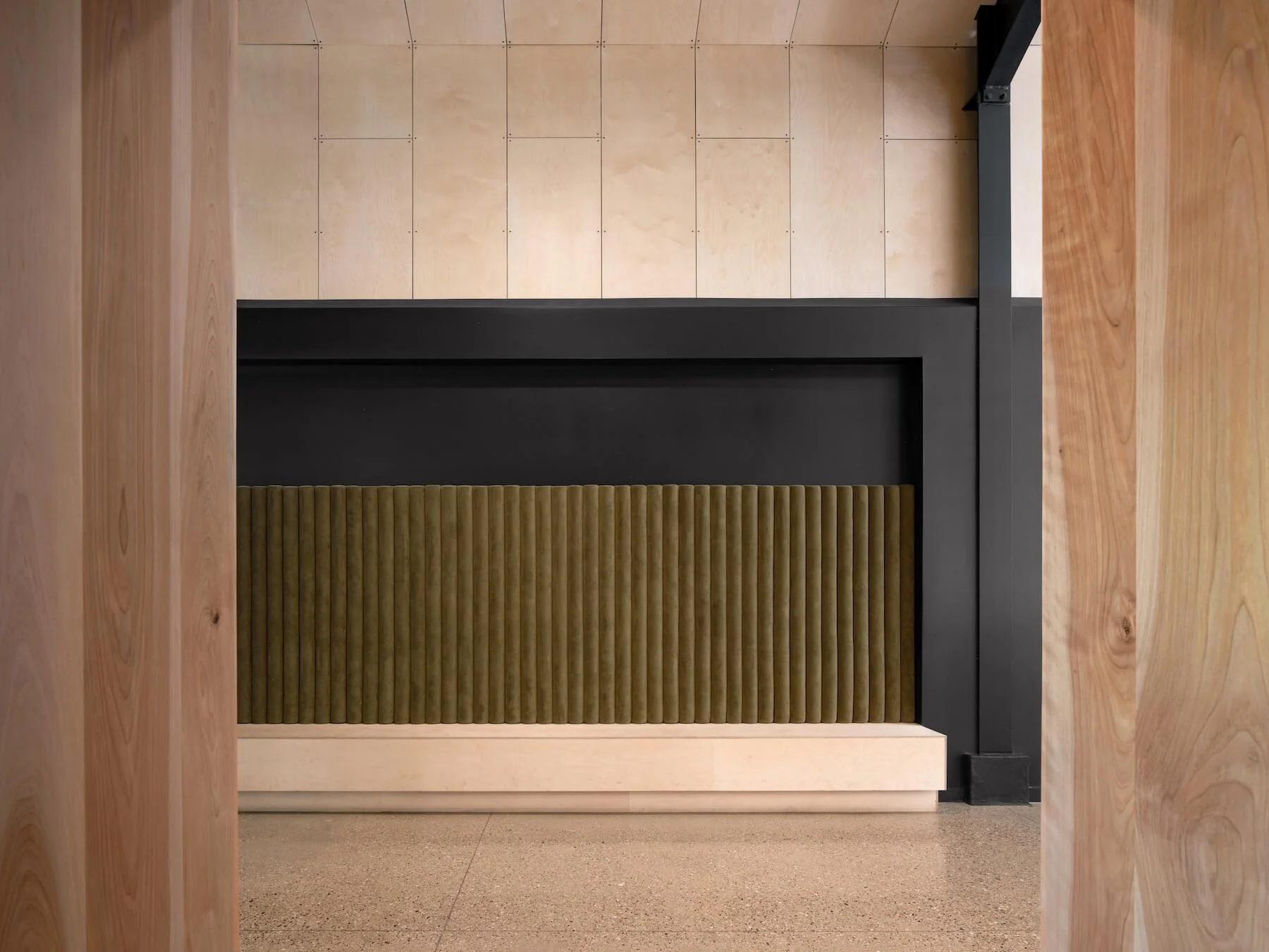 View through doorway revealing interior decor with wood panel walls, black metal framing, and beige upholstered furniture with vertical ridges.