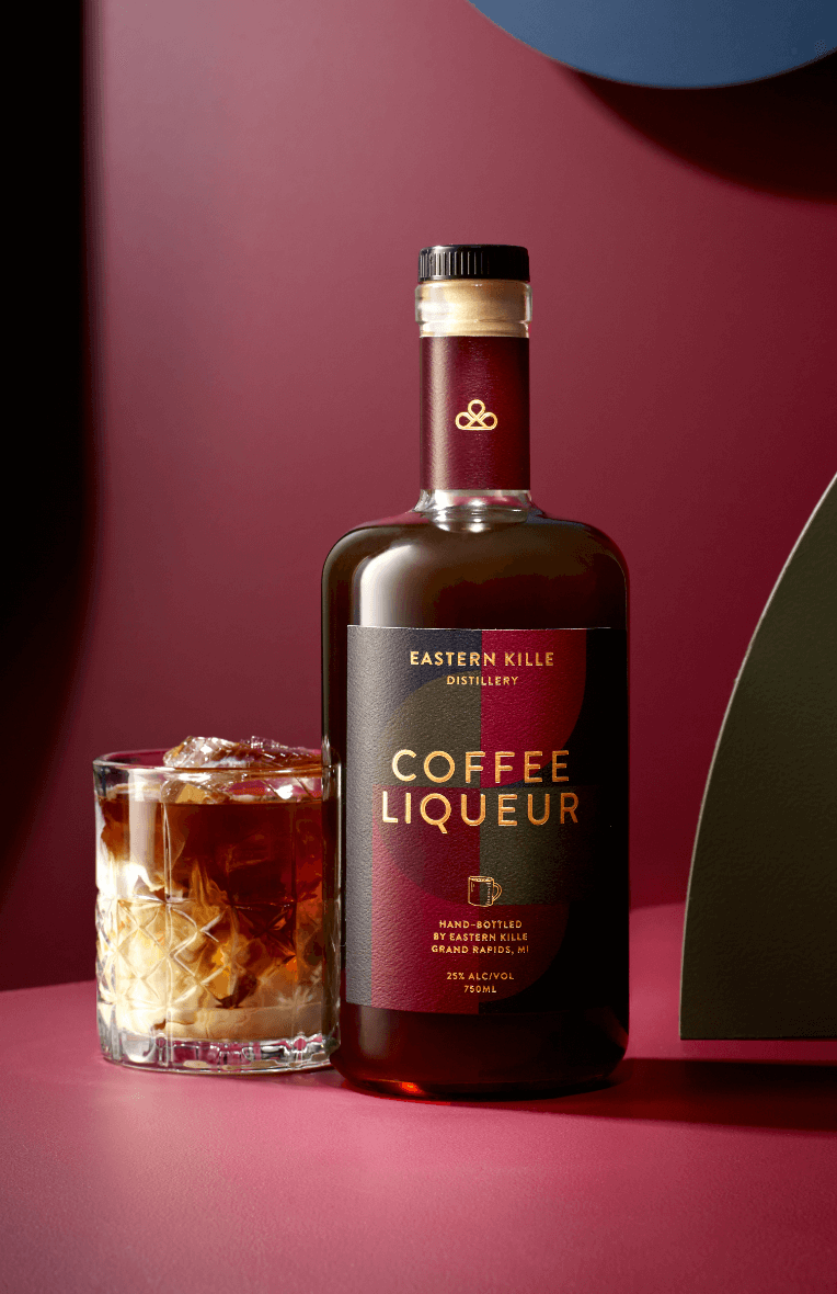 A bottle of Eastern Kille Coffee Liqueur next to a glass filled with ice and dark liquid, set against a pink and dark background.