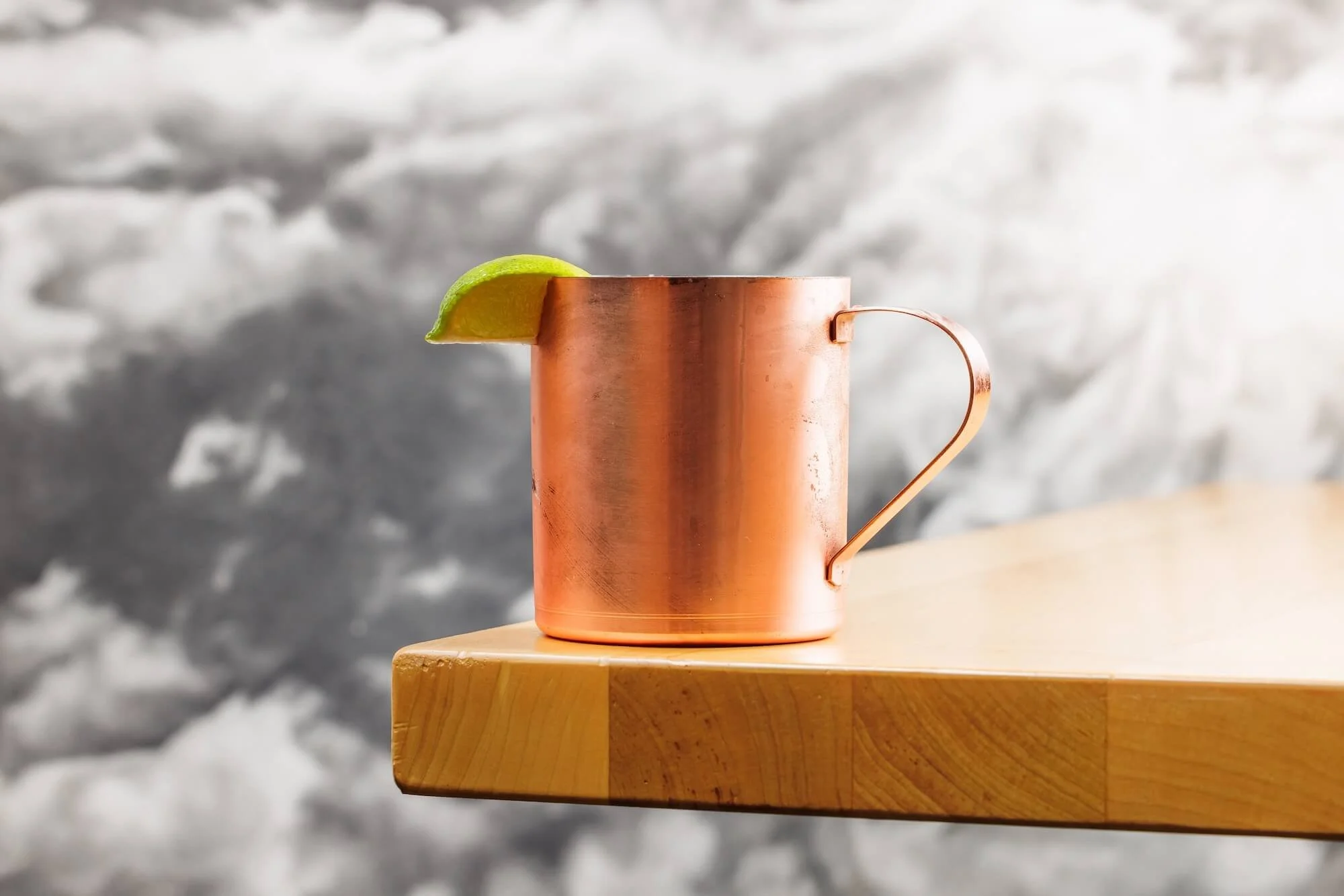 Copper mug with a lime wedge on the rim, placed on a wooden surface with snow in the background.