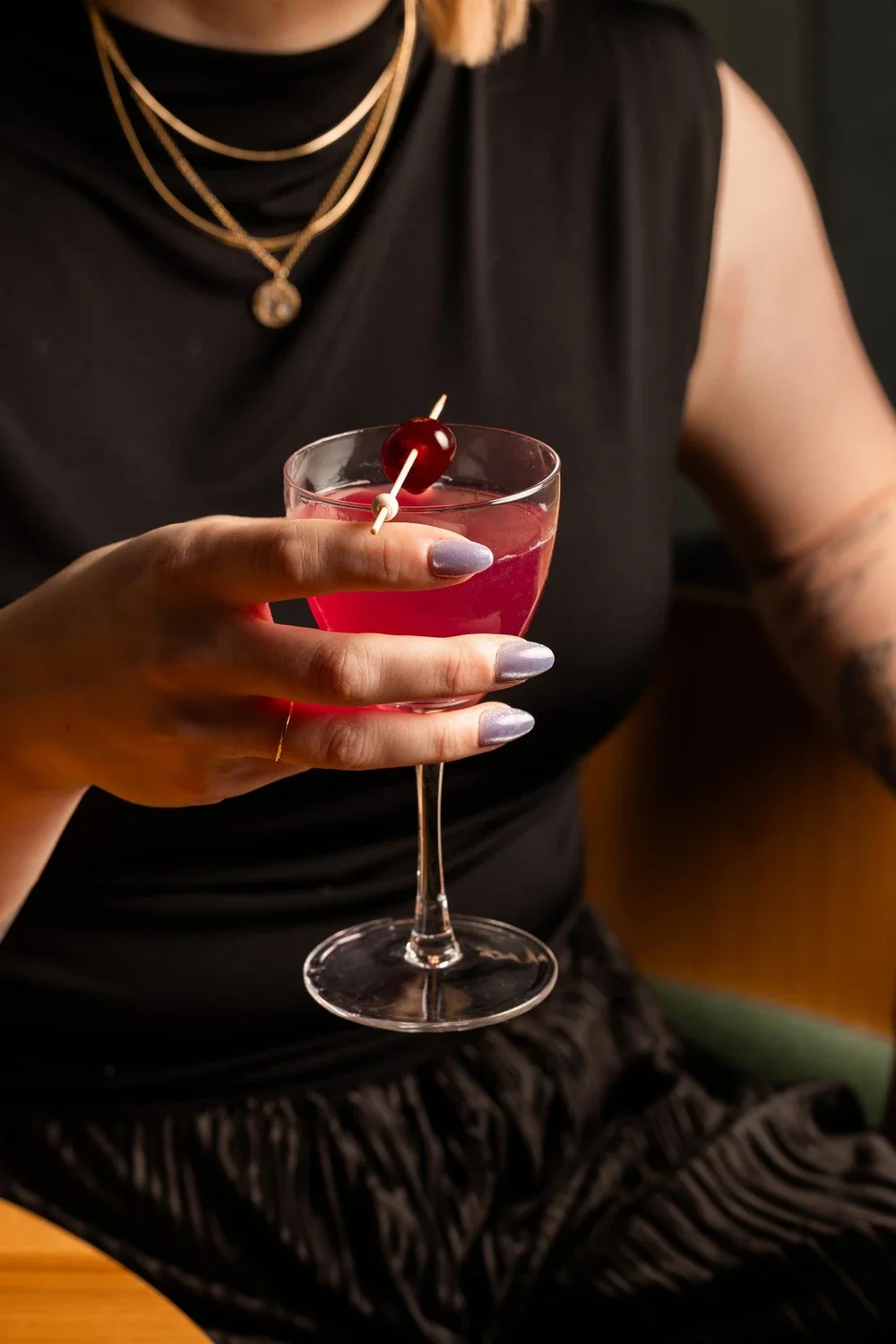 A woman holding a pink cocktail with a cherry garnish in a martini glass.