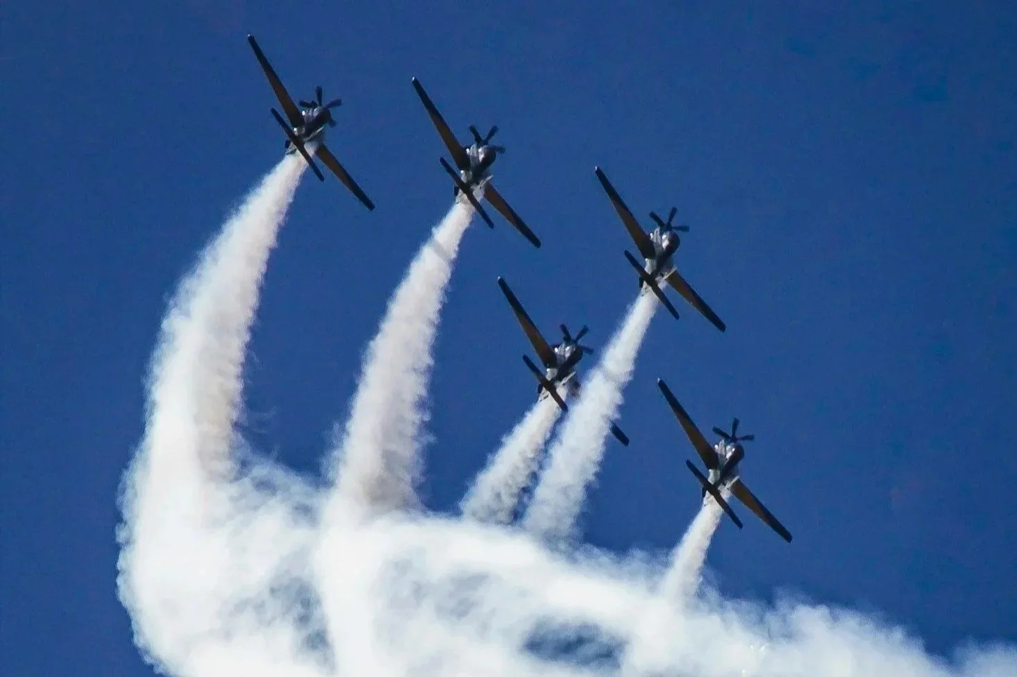 Five planes flying in formation in a clear blue sky, leaving white smoke trails.