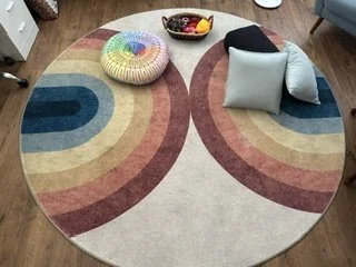 Colorful circular rug on a wooden floor with pillows and a bowl of fruit