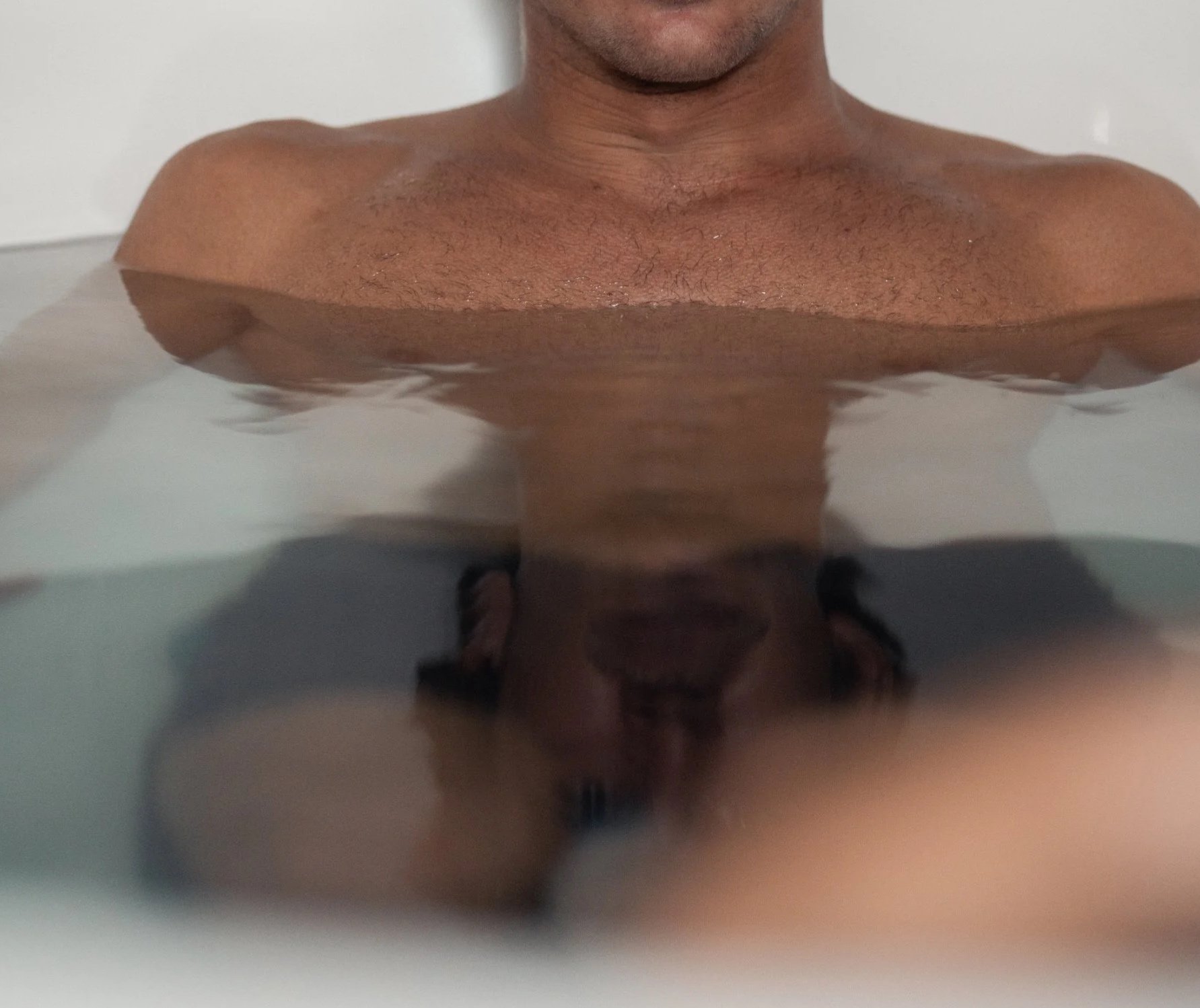 A person soaking in a bath with water partially covering their chest and lower face visible.