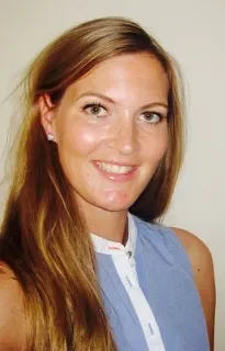 A woman with long red hair smiling at the camera, wearing a blue sleeveless top.