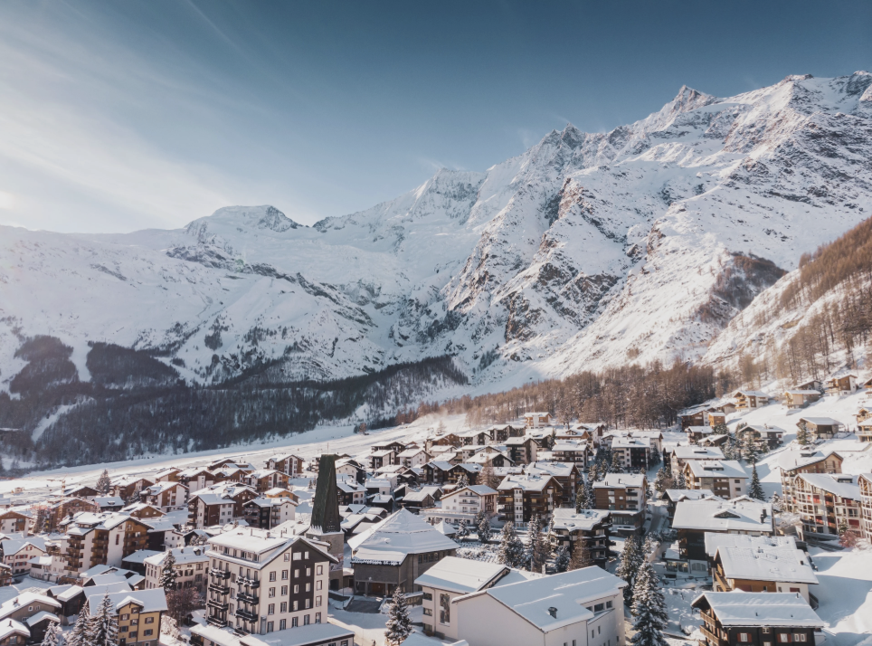 A snow-covered mountain village at the base of towering, snow-capped mountains during daytime.