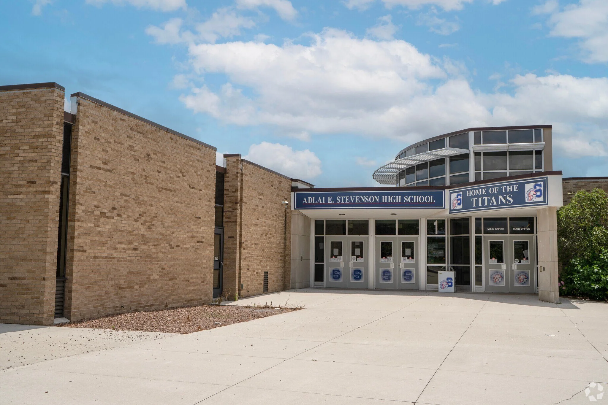 Exterior of Adlai E. Stevenson High School with a sign indicating it as the home of the Titans, showing a clear sky and doors with school logos.