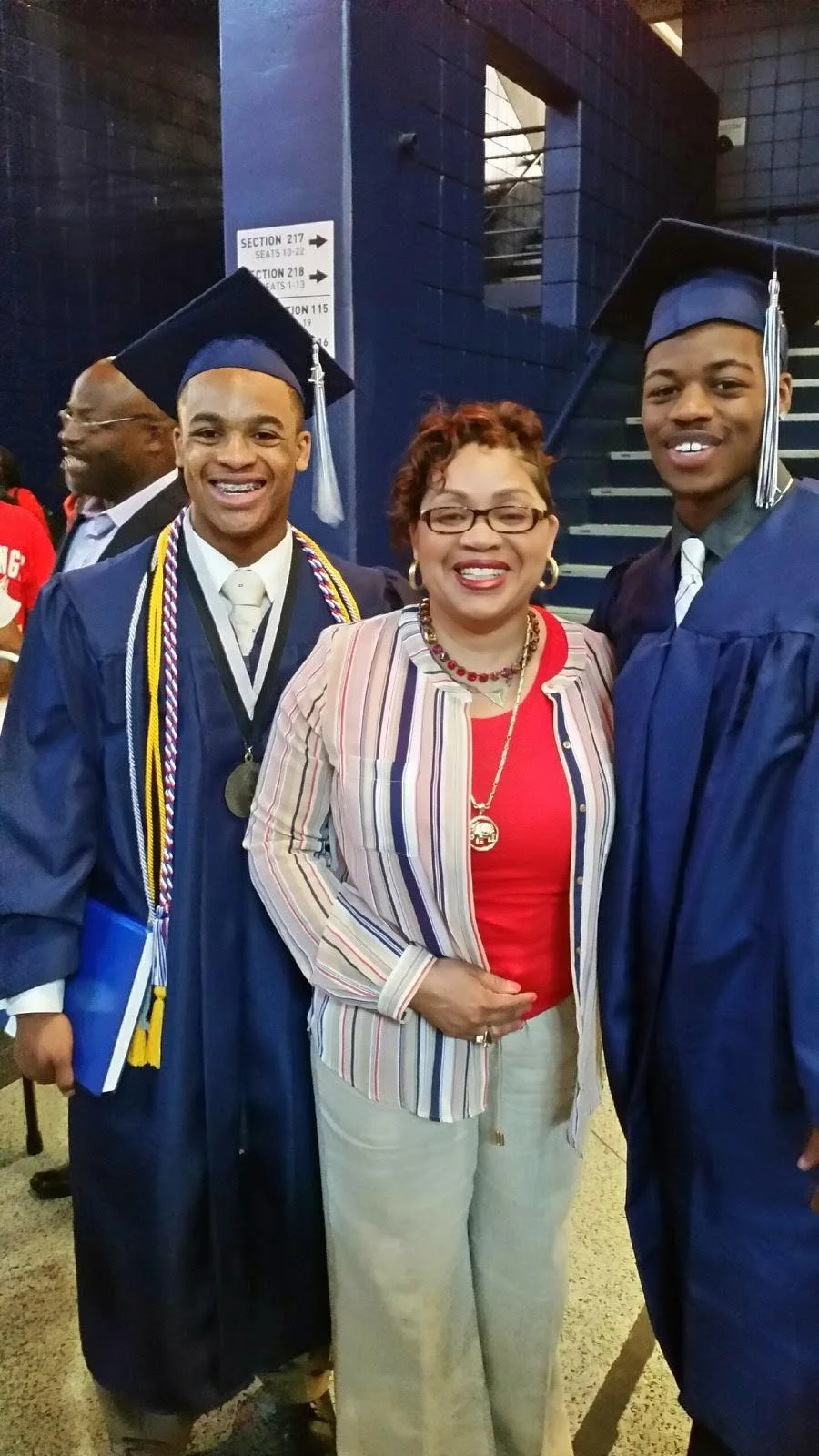Three graduates in caps and gowns with a woman in a striped blazer at a graduation ceremony.