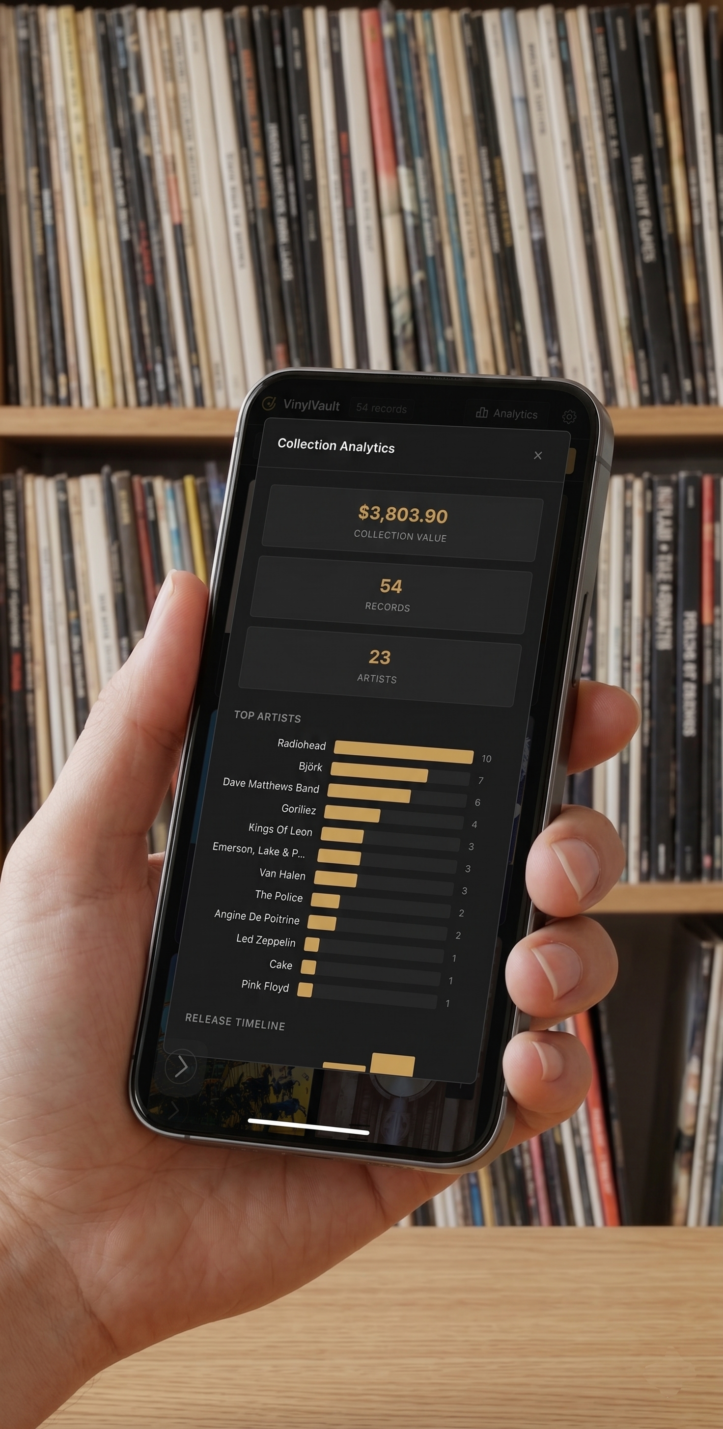 Person holding a smartphone displaying vinyl collection analytics, with shelves of records in the background.