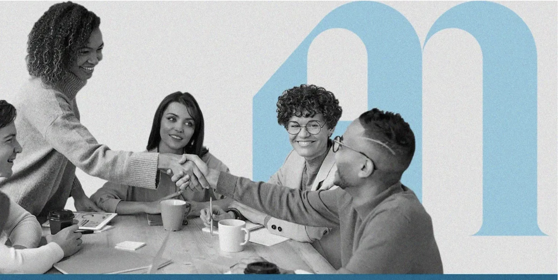 Group of five diverse people at a meeting table, exchanging a handshake with a large blue letter 'm' on the wall behind them.