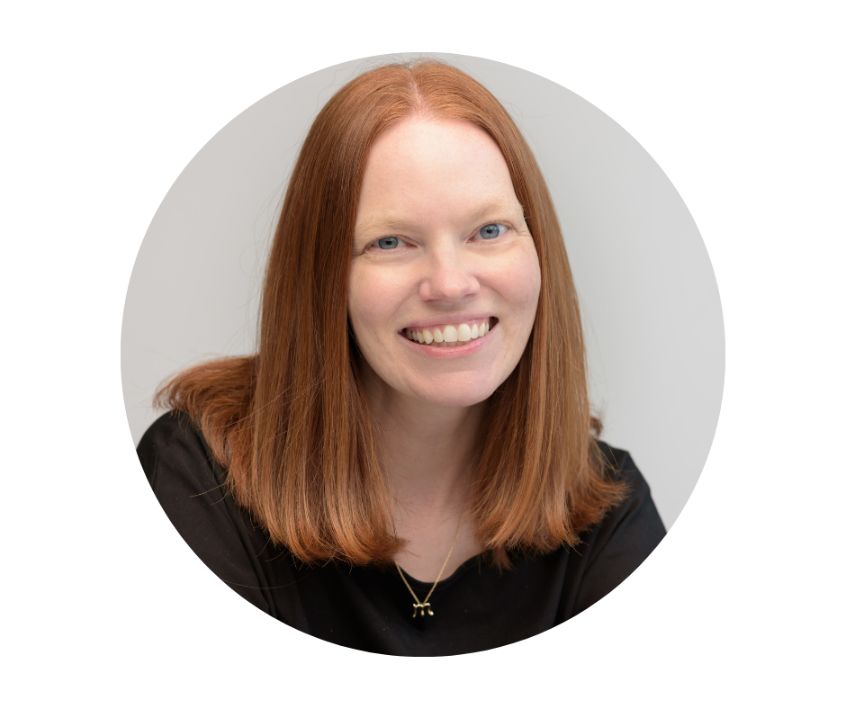 A woman with long red hair, blue eyes, and a black top smiling at the camera against a plain light background.