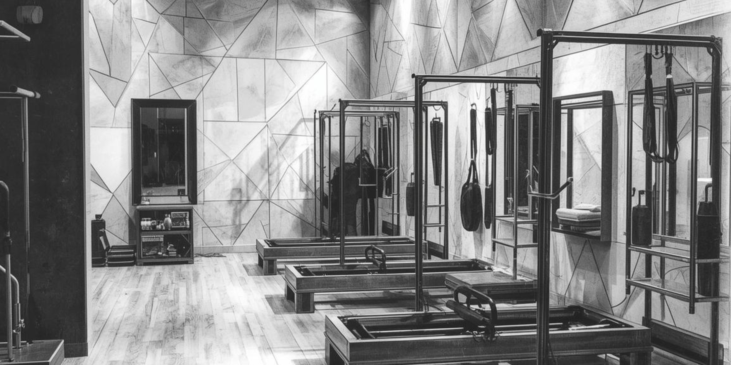 Interior of a fitness or Pilates studio with reformer machines positioned in rows, mirrors on the wall, and geometric wall patterns.