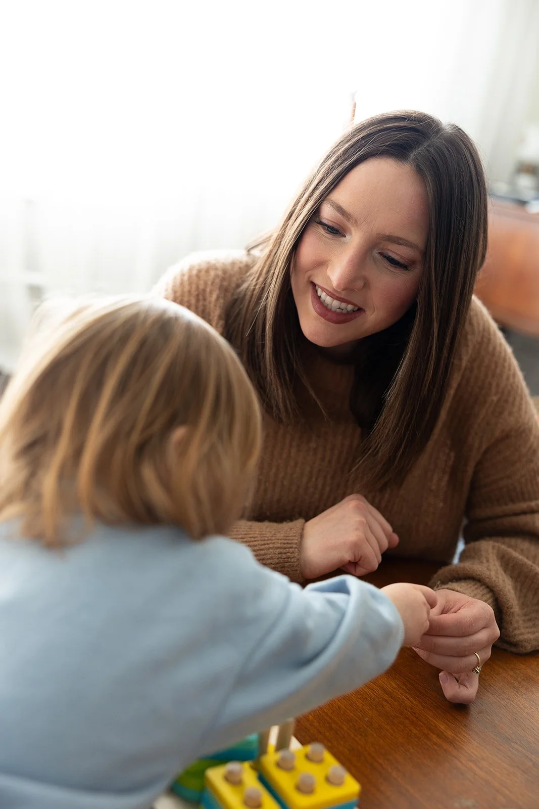 A woman smiling and engaging with a young girl at a table, with a colorful toy in front of them.
