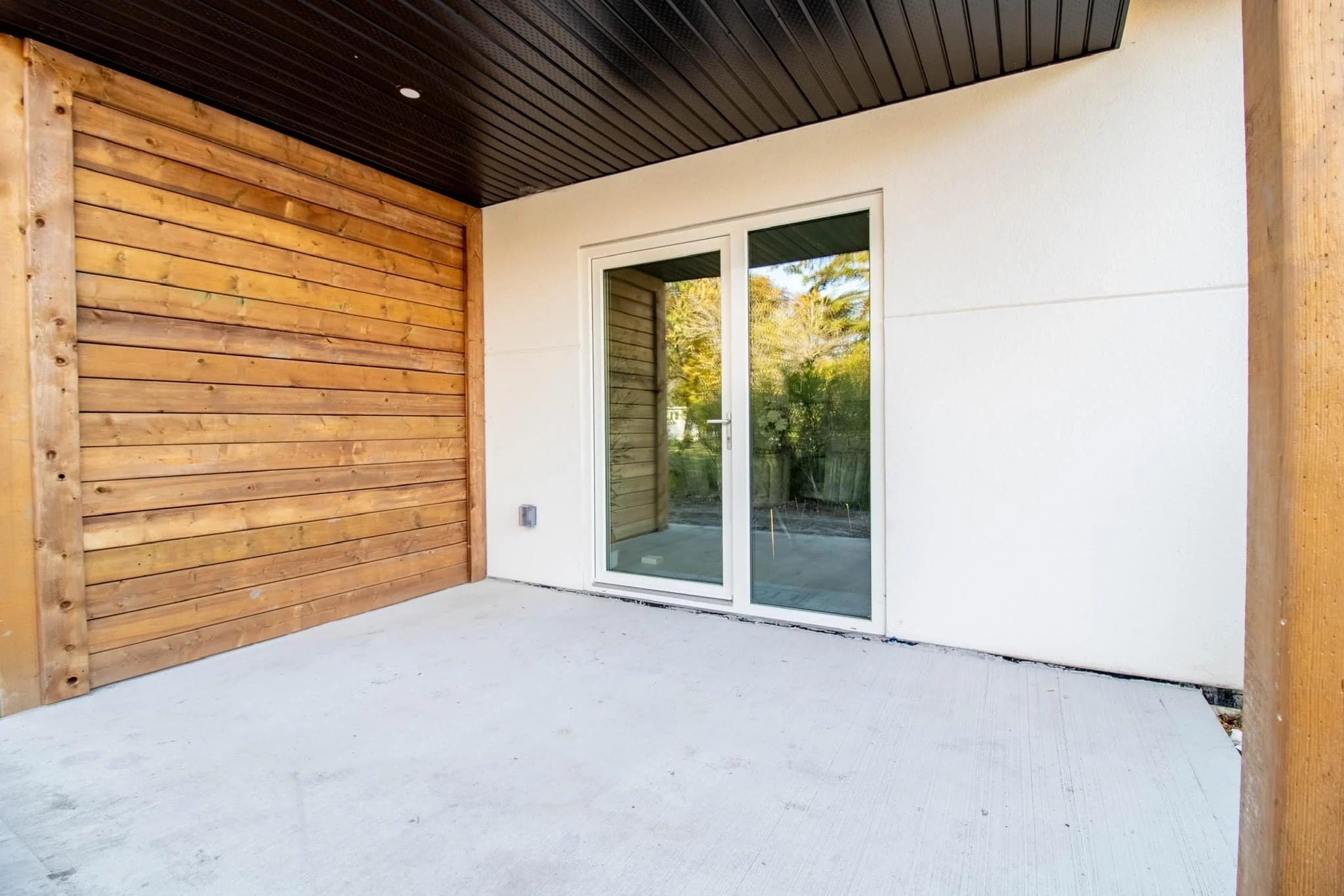 Empty patio with concrete flooring, wooden wall, glass sliding door, and black ceiling panels.