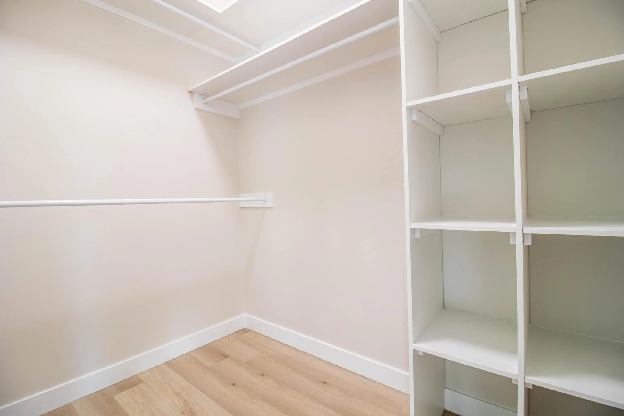 Empty walk-in closet with white walls, wood flooring, and built-in white shelving units.