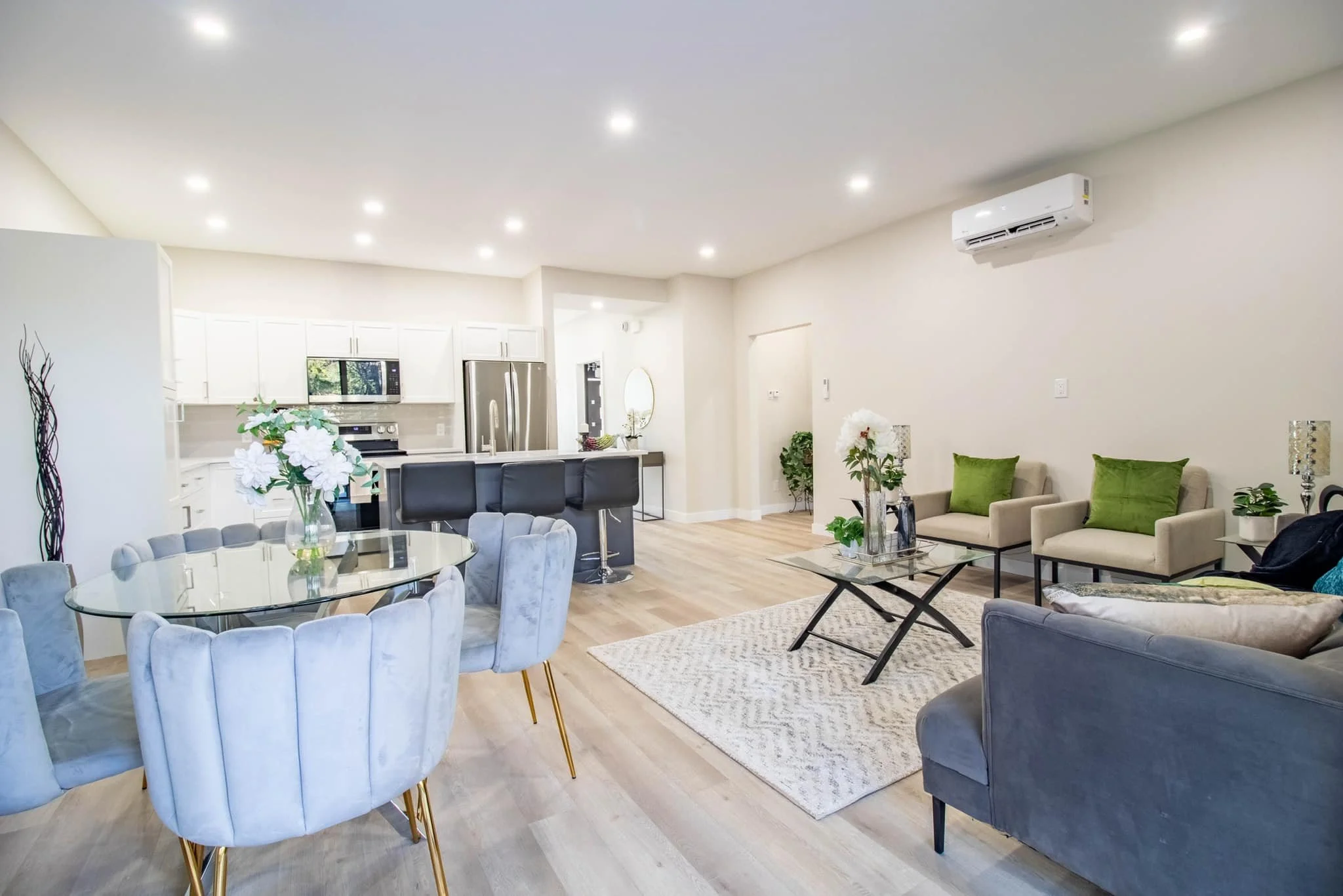 Open-concept living room and kitchen with modern furniture, white walls, wooden floors, and multiple ceiling lights.