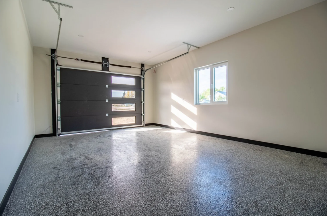 Empty garage with a black sectional garage door, a window on the right wall, and a speckled gray epoxy floor.