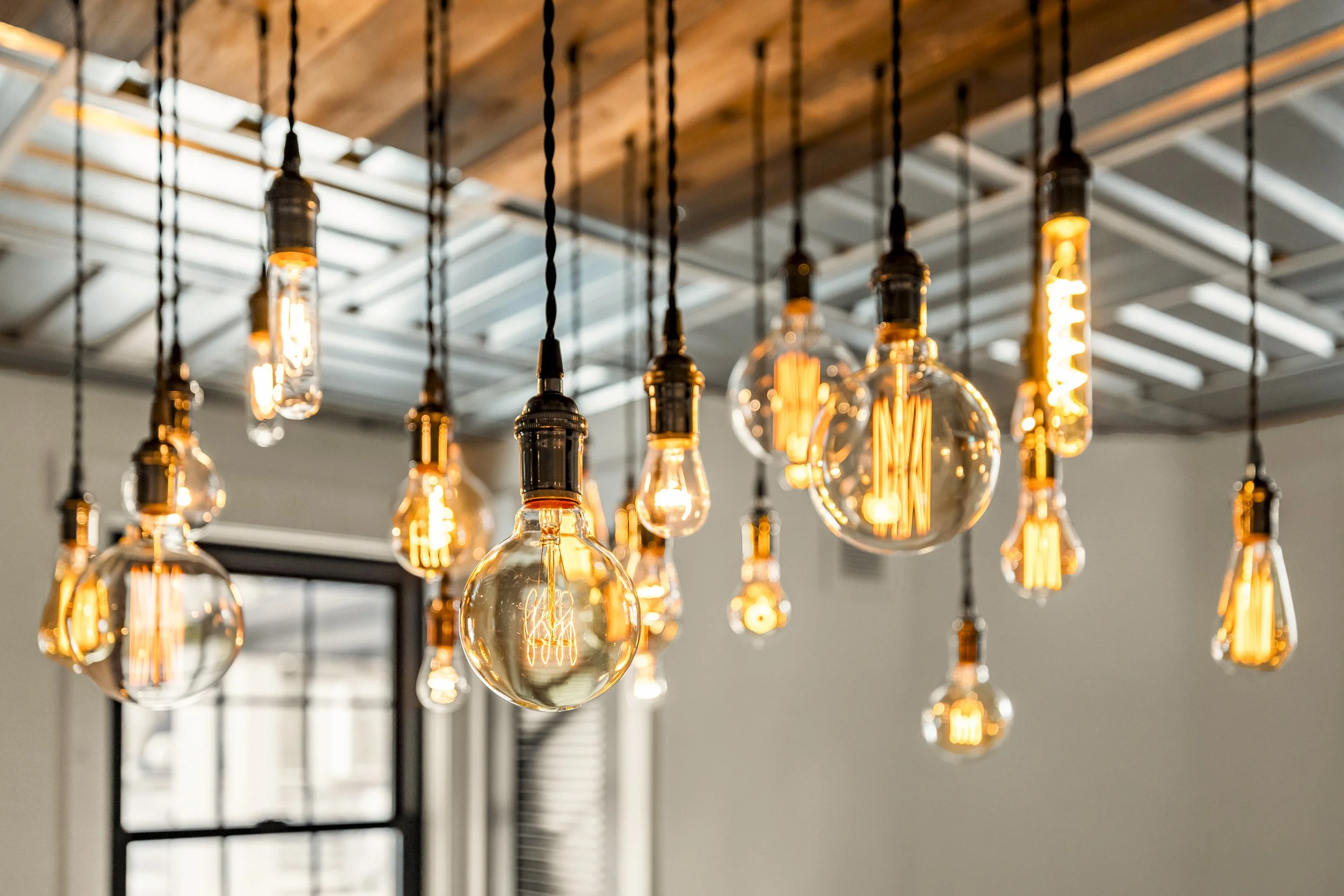 A modern ceiling with multiple vintage-style Edison light bulbs hanging from black cords, some of which are on and glowing.