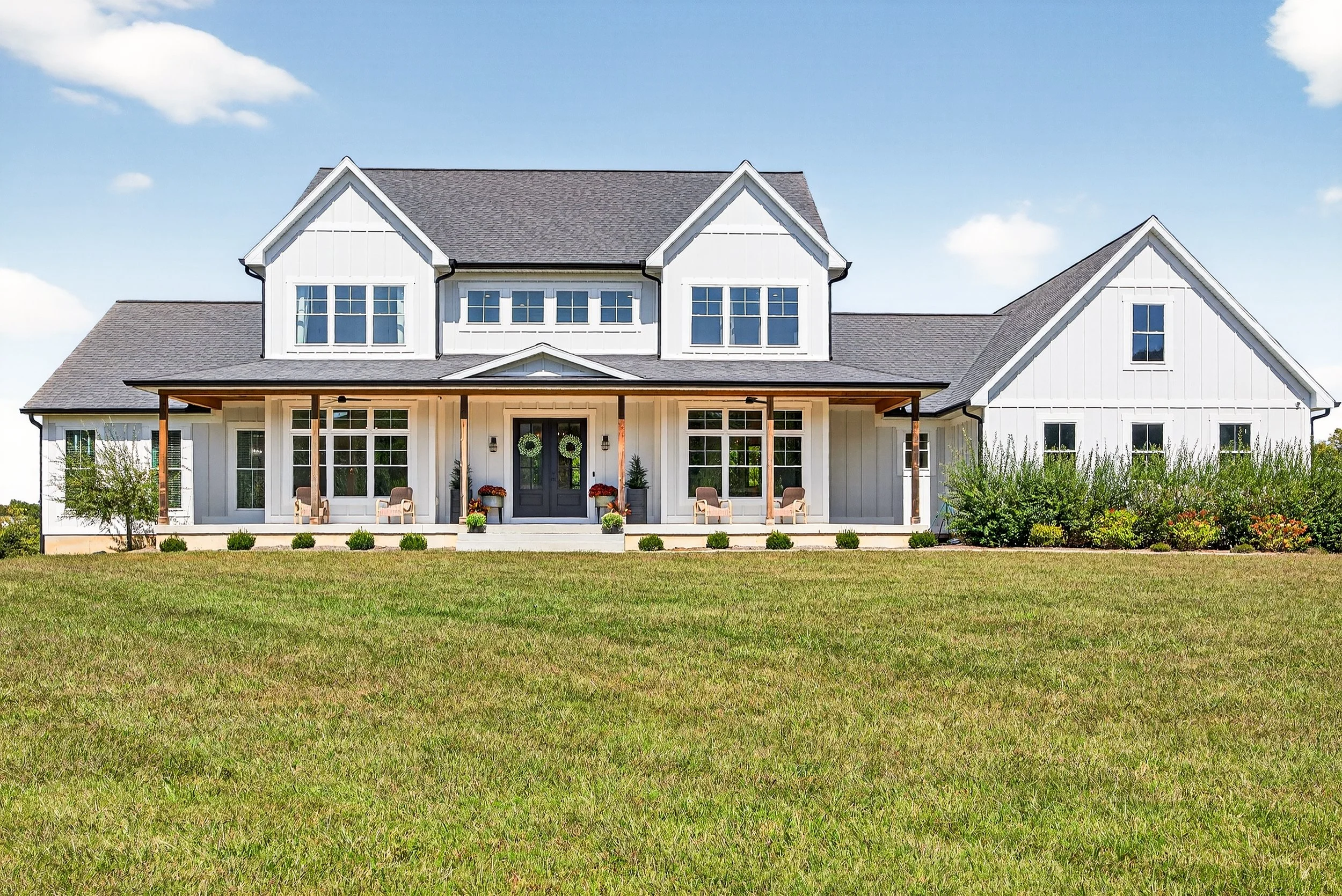 A modern white house with a front porch, gray roof, and multiple windows, set on a grassy lawn under a blue sky.