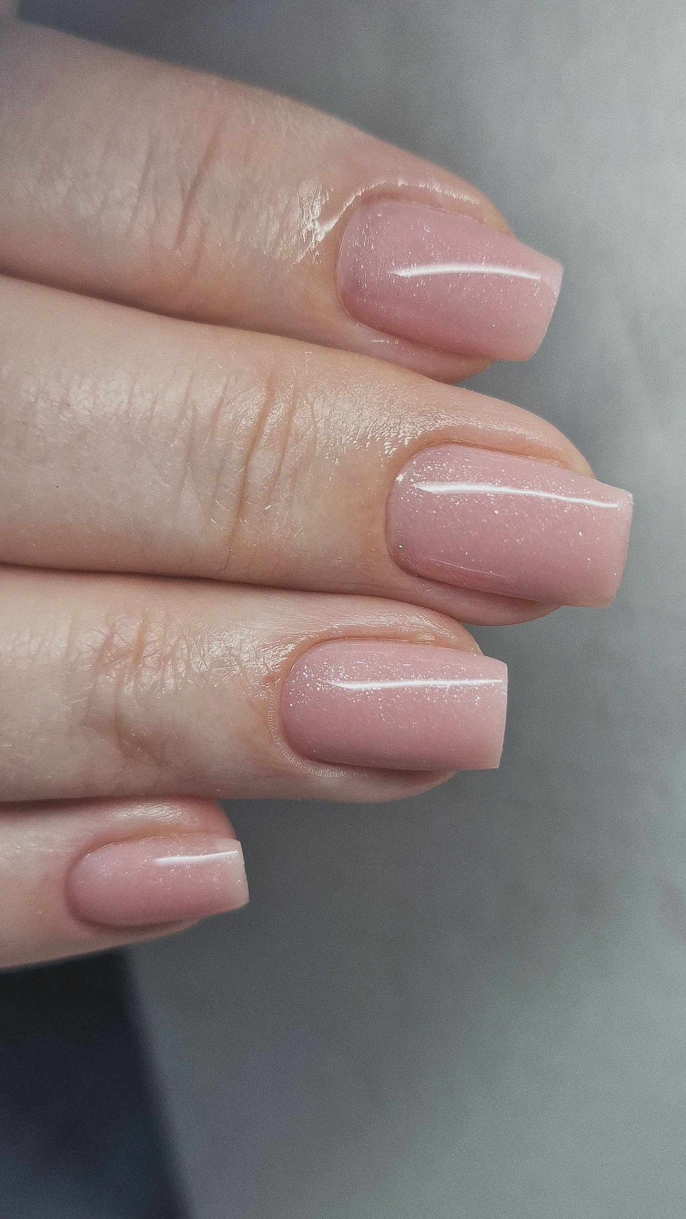 Close-up of a hand with manicured nails painted in a soft pink shade with a subtle glittery finish.