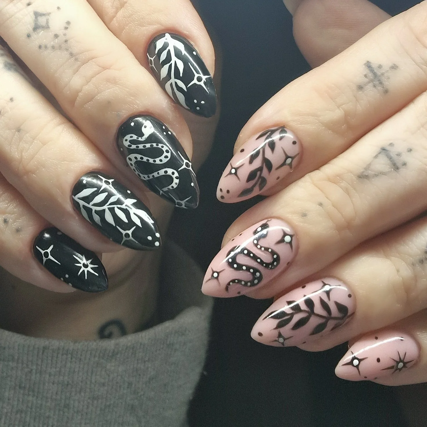 Nail art with black and pale pink base colors featuring white and black intricate leaf, star, dot, and snake-like designs.