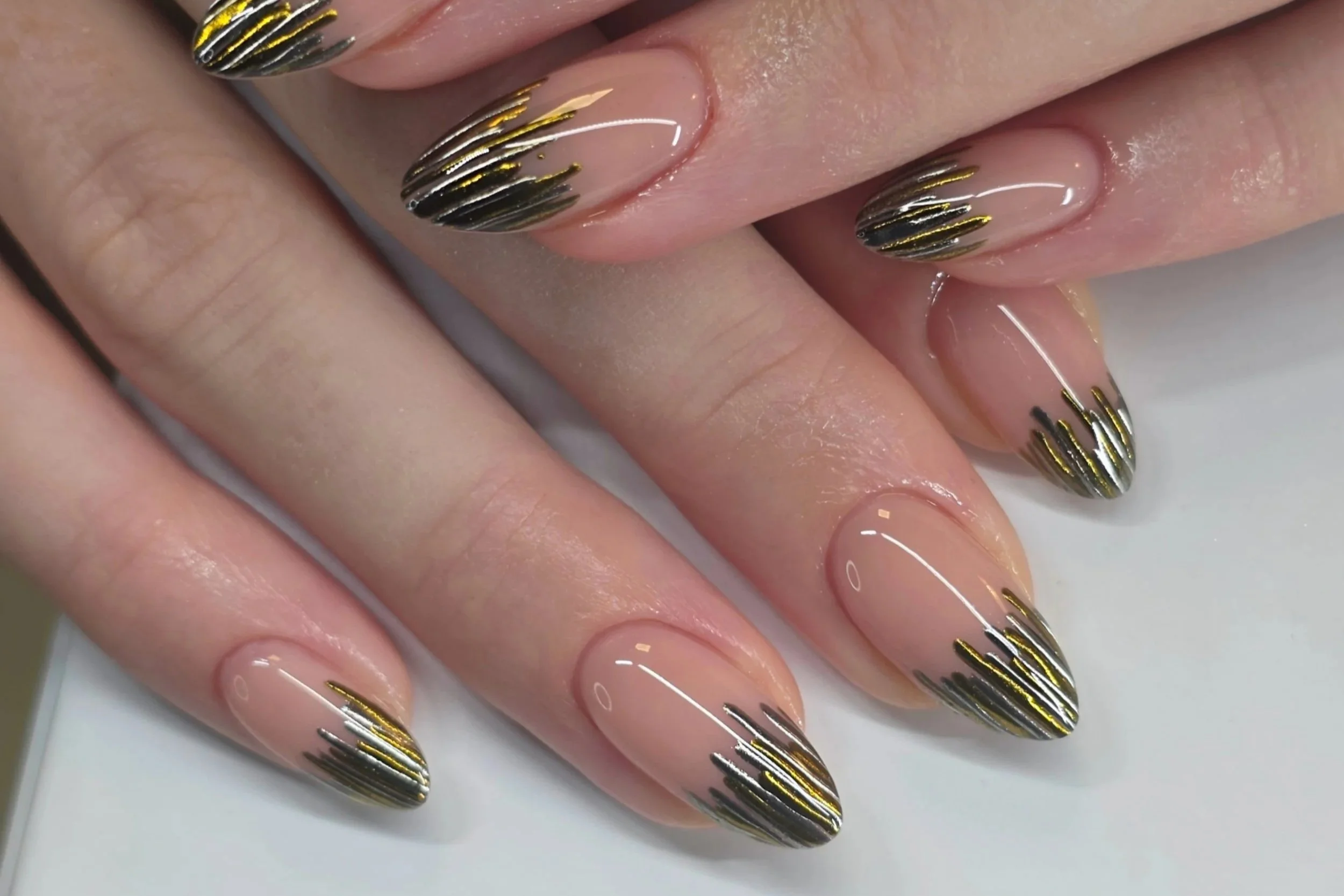 Close-up of builder gel manicured nails with a nude base and black and gold isolated chrome striped tips.