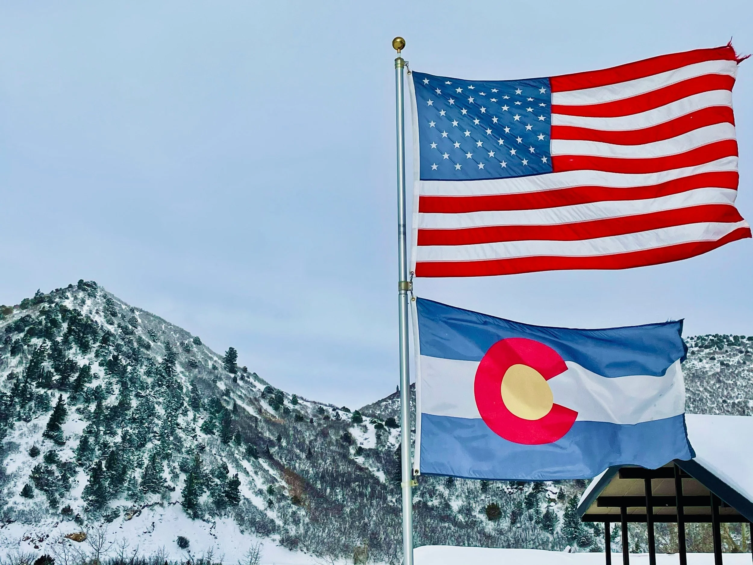 American flag flying in front of snowy mountain landscape on a cloudy day.