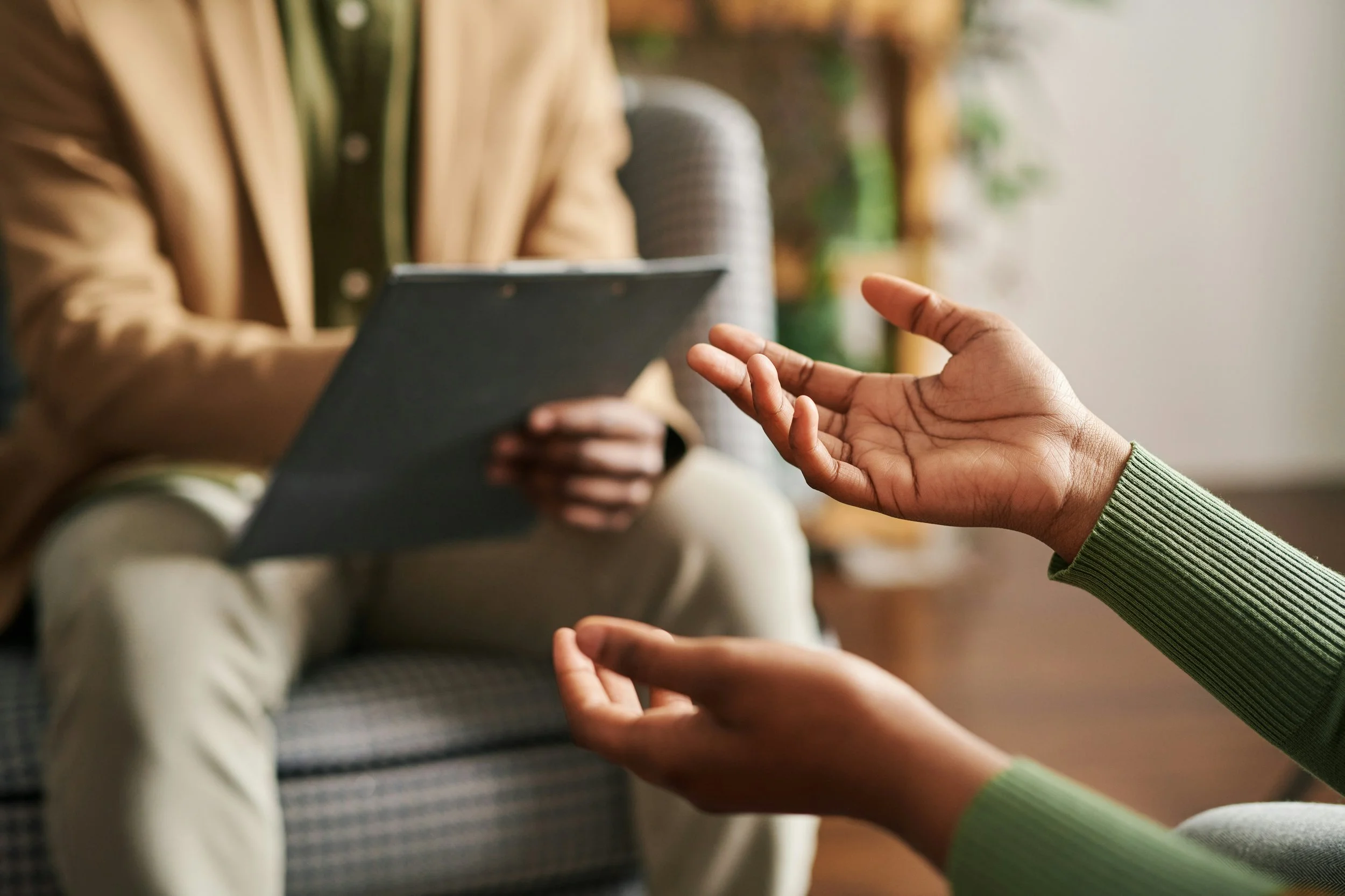Two people having a conversation, one using hand gestures, with a tablet in the background.