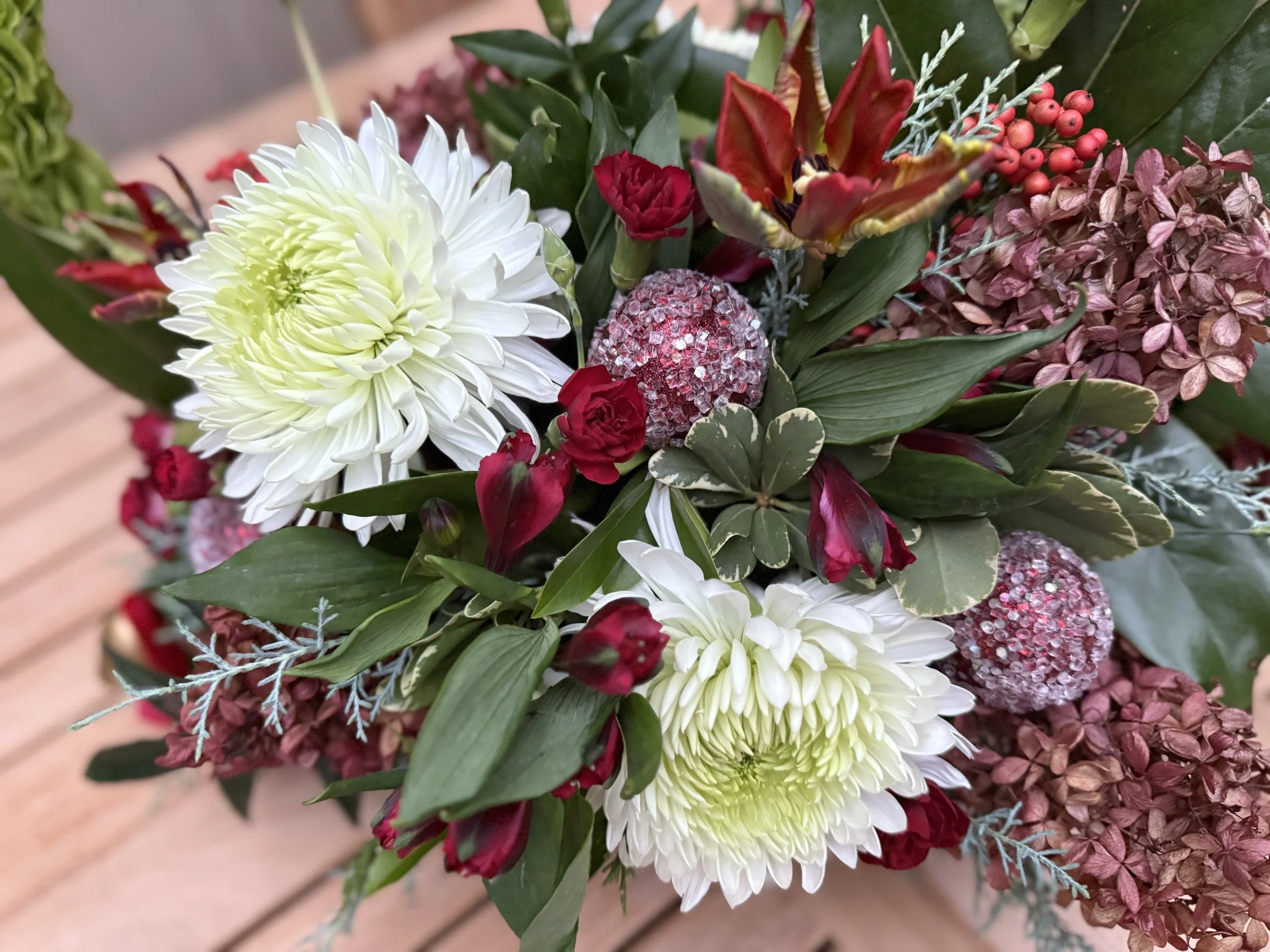 A bouquet of flowers including white chrysanthemums, red roses, pink hydrangeas, and various green and red foliage.