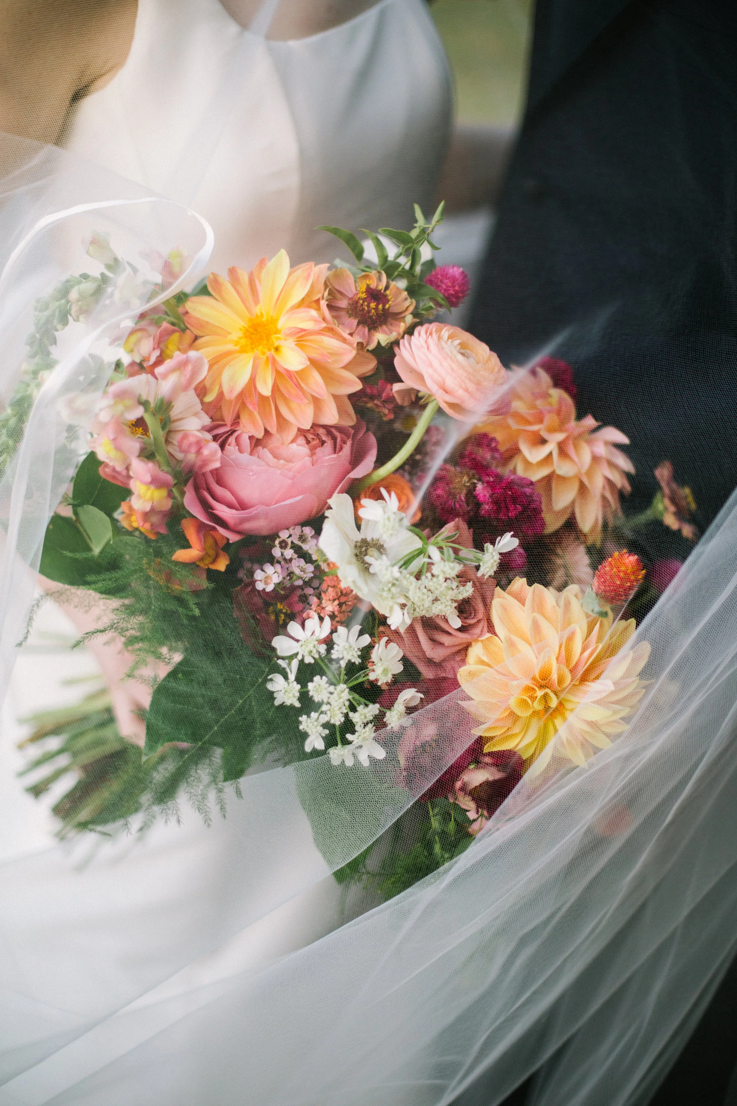 A bouquet of pink, orange, and white flowers wrapped in sheer white tulle.