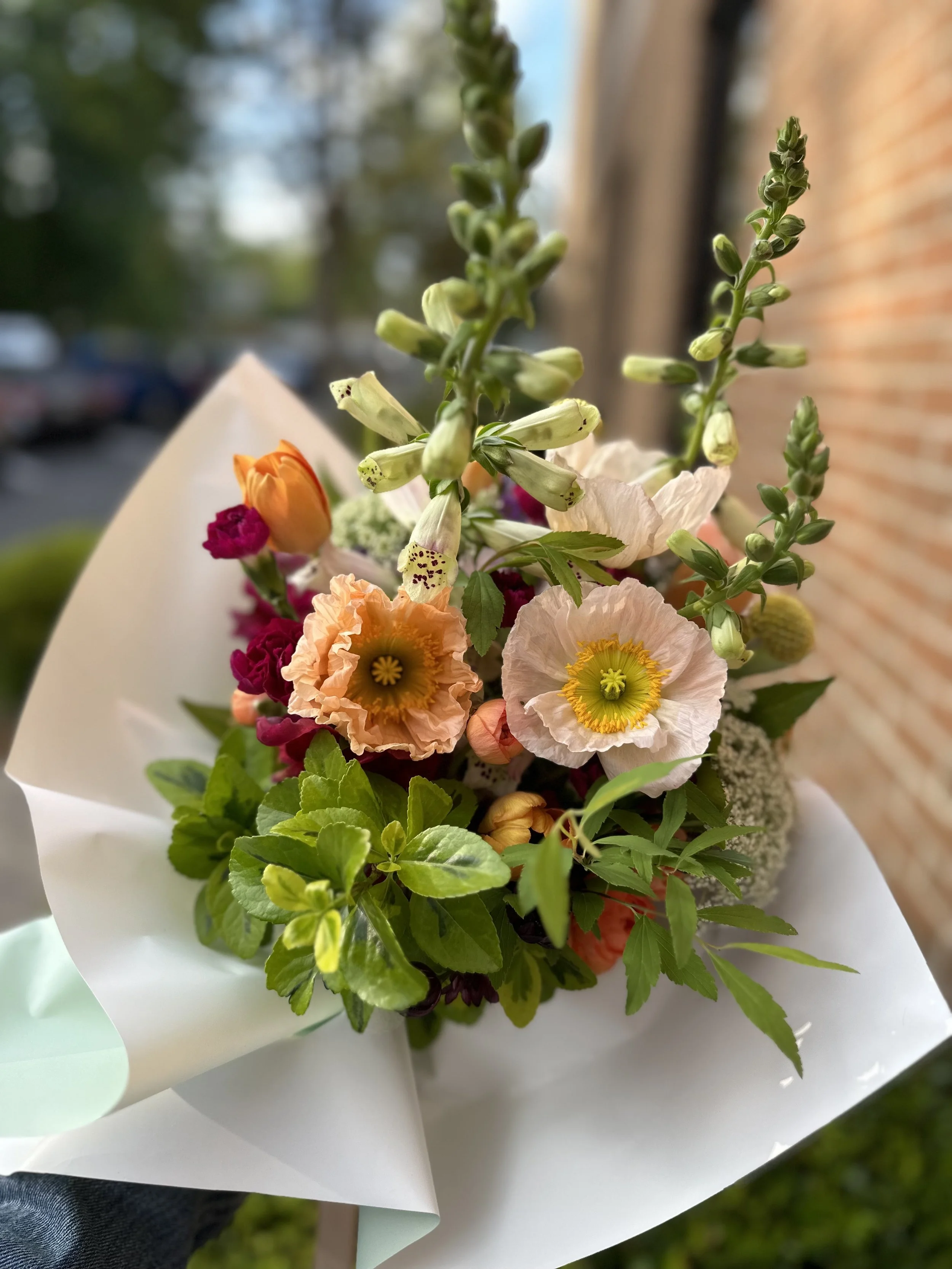 Colorful bouquet of flowers including poppies, lilies, and various greenery wrapped in white paper.