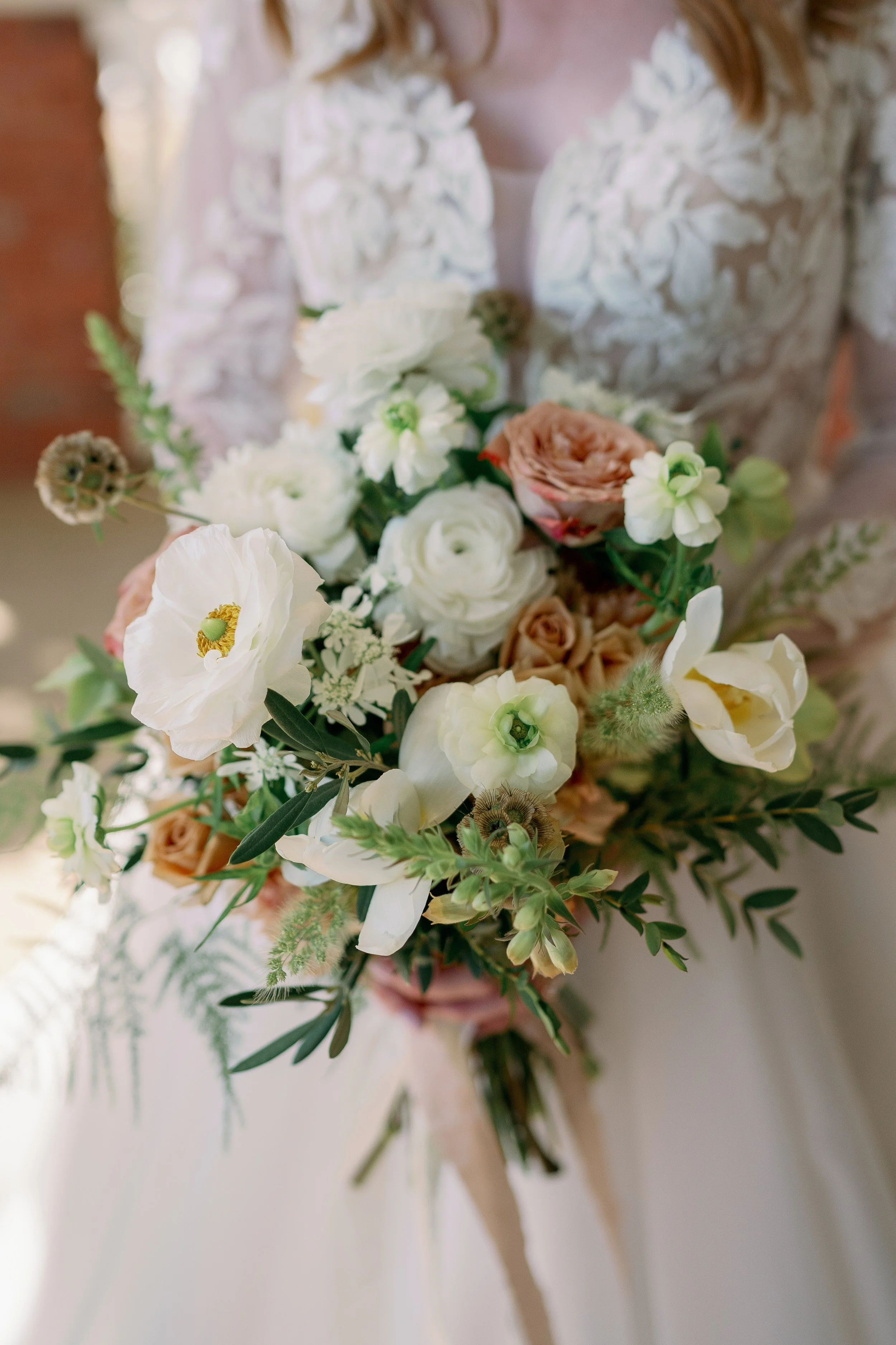 Bride holding a bouquet of white, cream, and blush pink flowers, with greenery and floral accents.