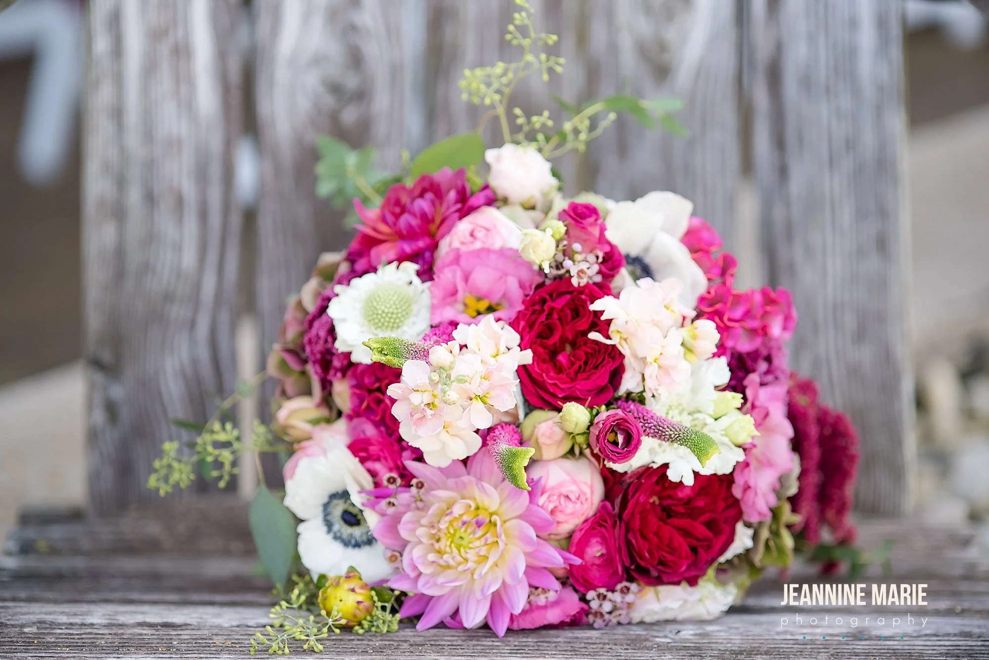 A colorful bouquet of pink, white, and red flowers resting on a rustic wooden surface with a weathered wooden background.