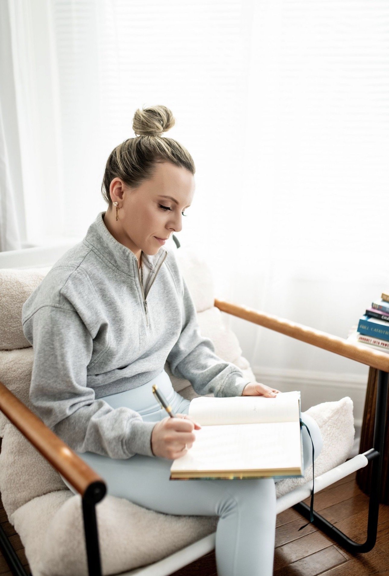 Picture of Lauren, owner of Lauren Daly Clark Yoga & Wellness, LLC.  Lauren is seated and writing in a journal.  She is wearing a gray cropped sweatshirt and light blue yoga pants.