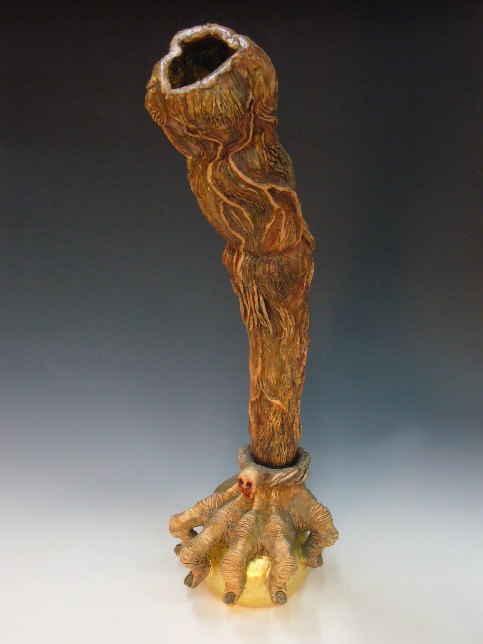 A wooden sculpture with a hollow top, a twisted, textured body, and animal-like feet on a round base.