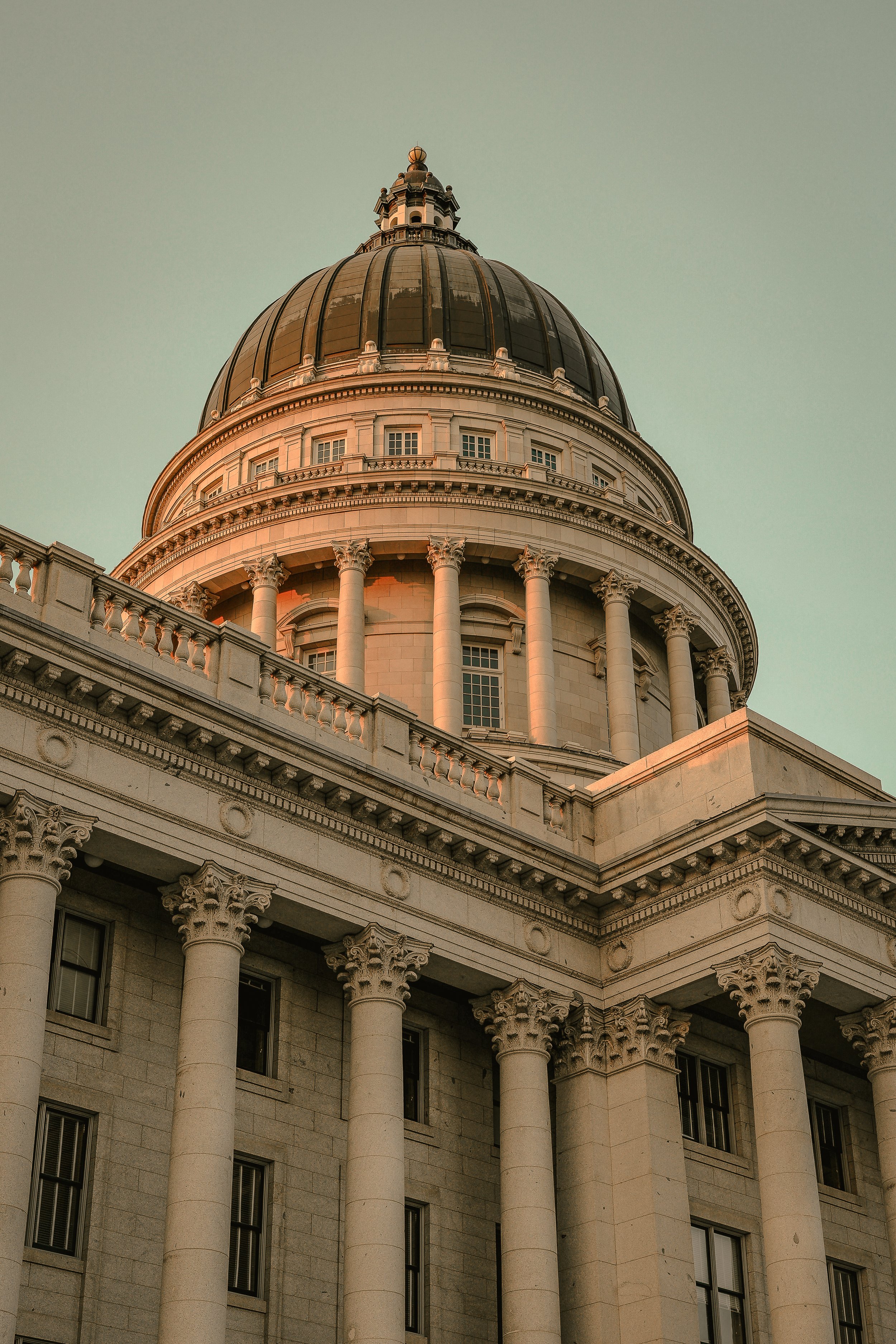 The dome of a government building with classical columns and detailed architectural features, illuminated by warm sunlight.