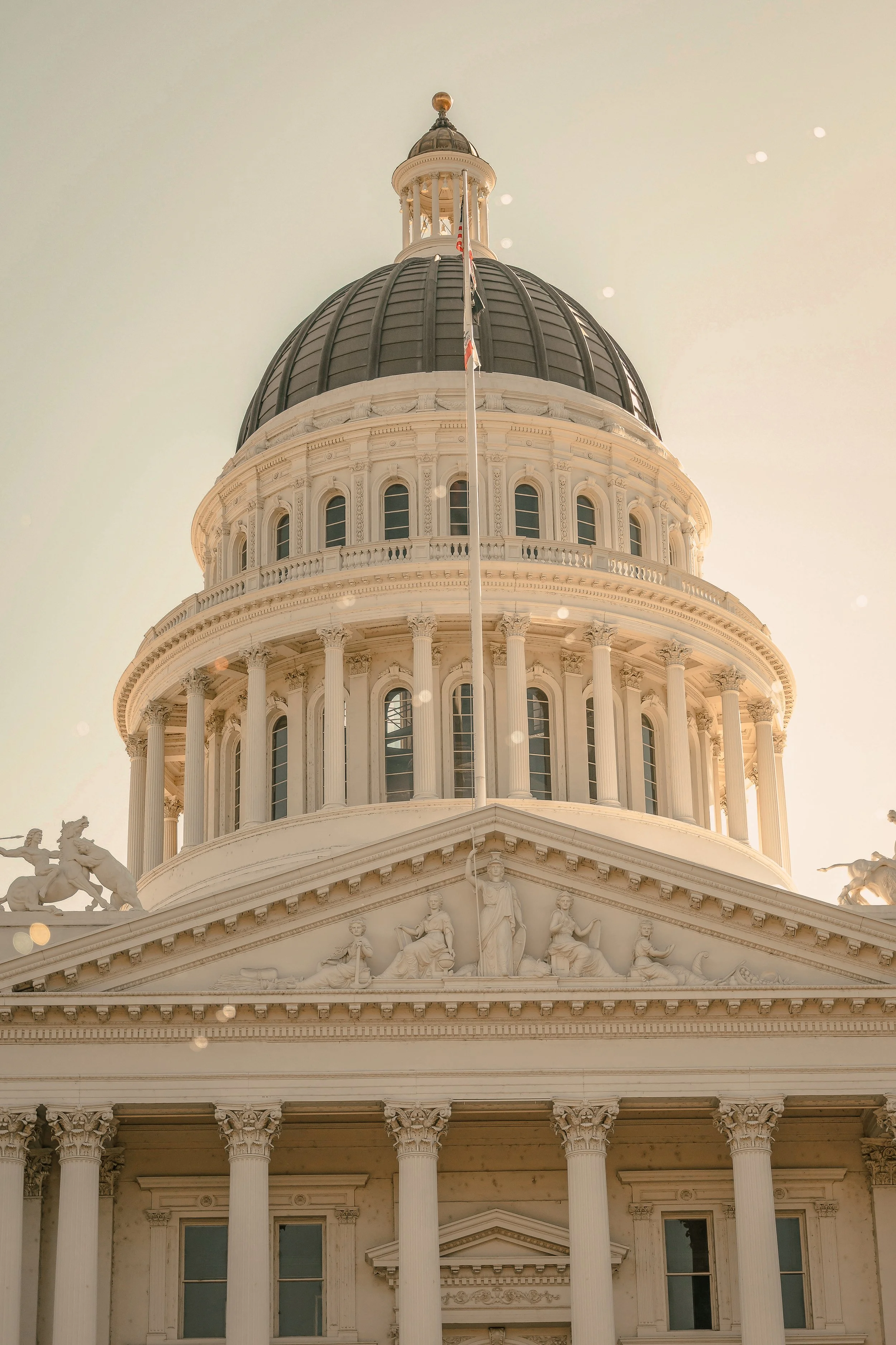 Front view of a historic government building with a large dome, columns, and detailed sculptures on the facade, under a clear sky.